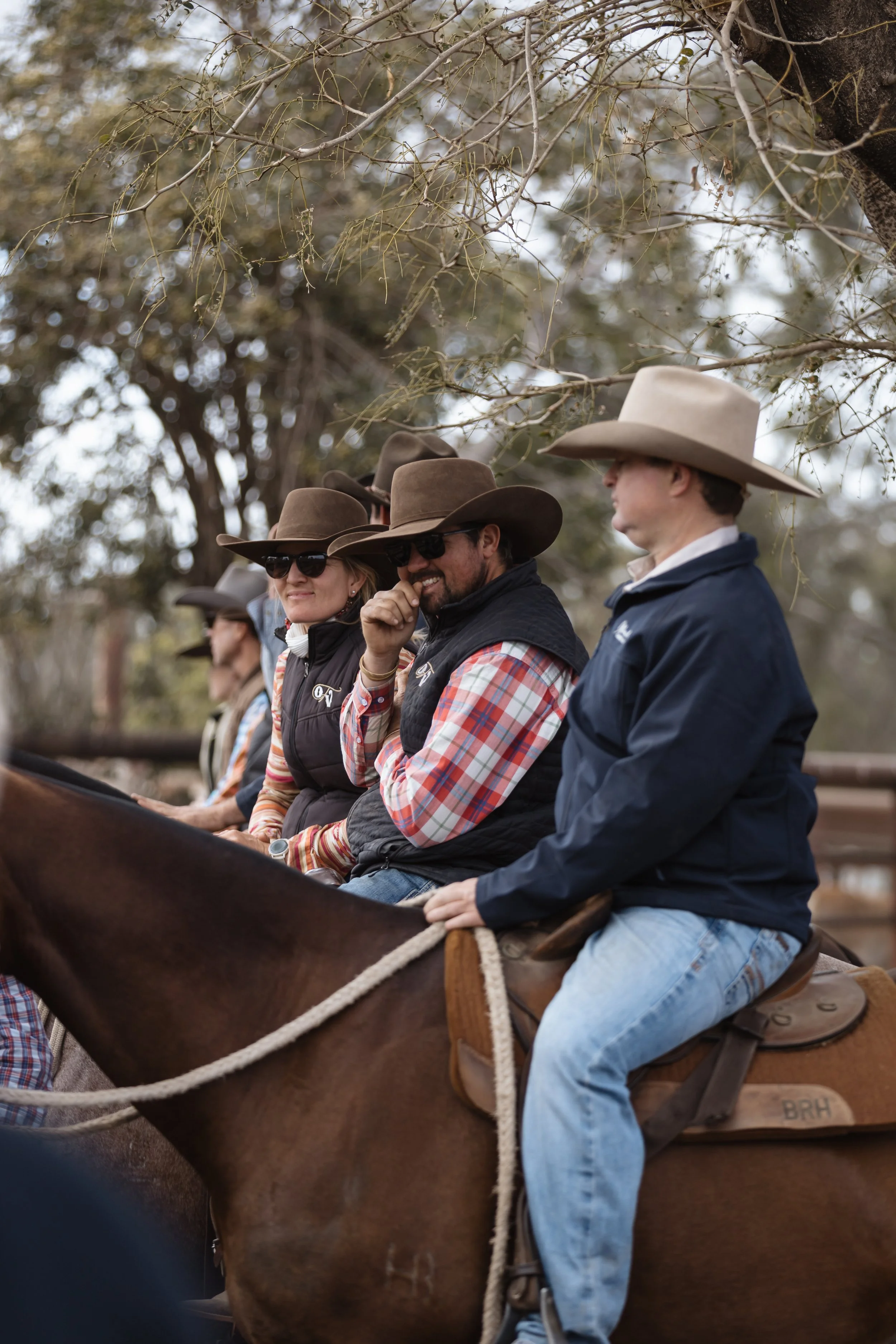Group of people riding horses outdoors, wearing cowboy hats and sunglasses.