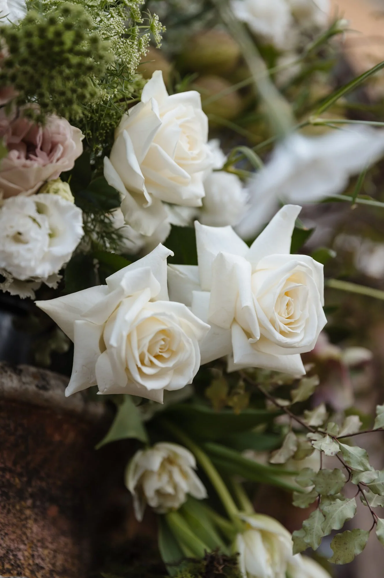 A bouquet of white roses with some greenery on a wooden surface.