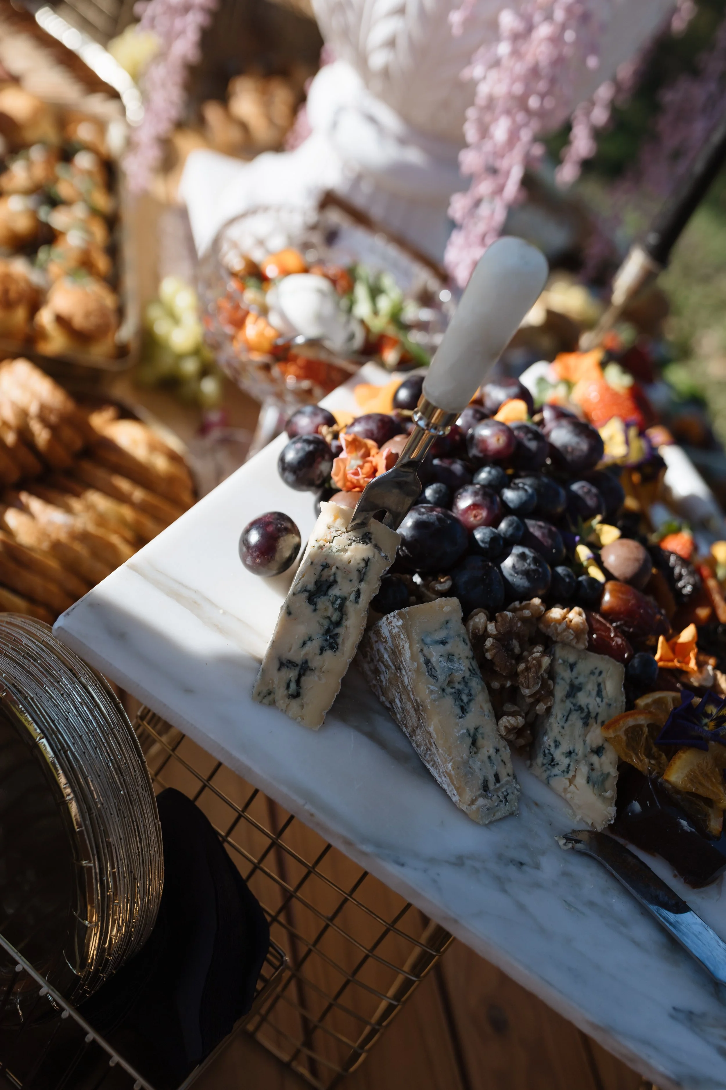A cheese platter featuring blue cheese wedges, black grapes, and various cheeses on a white marble board.