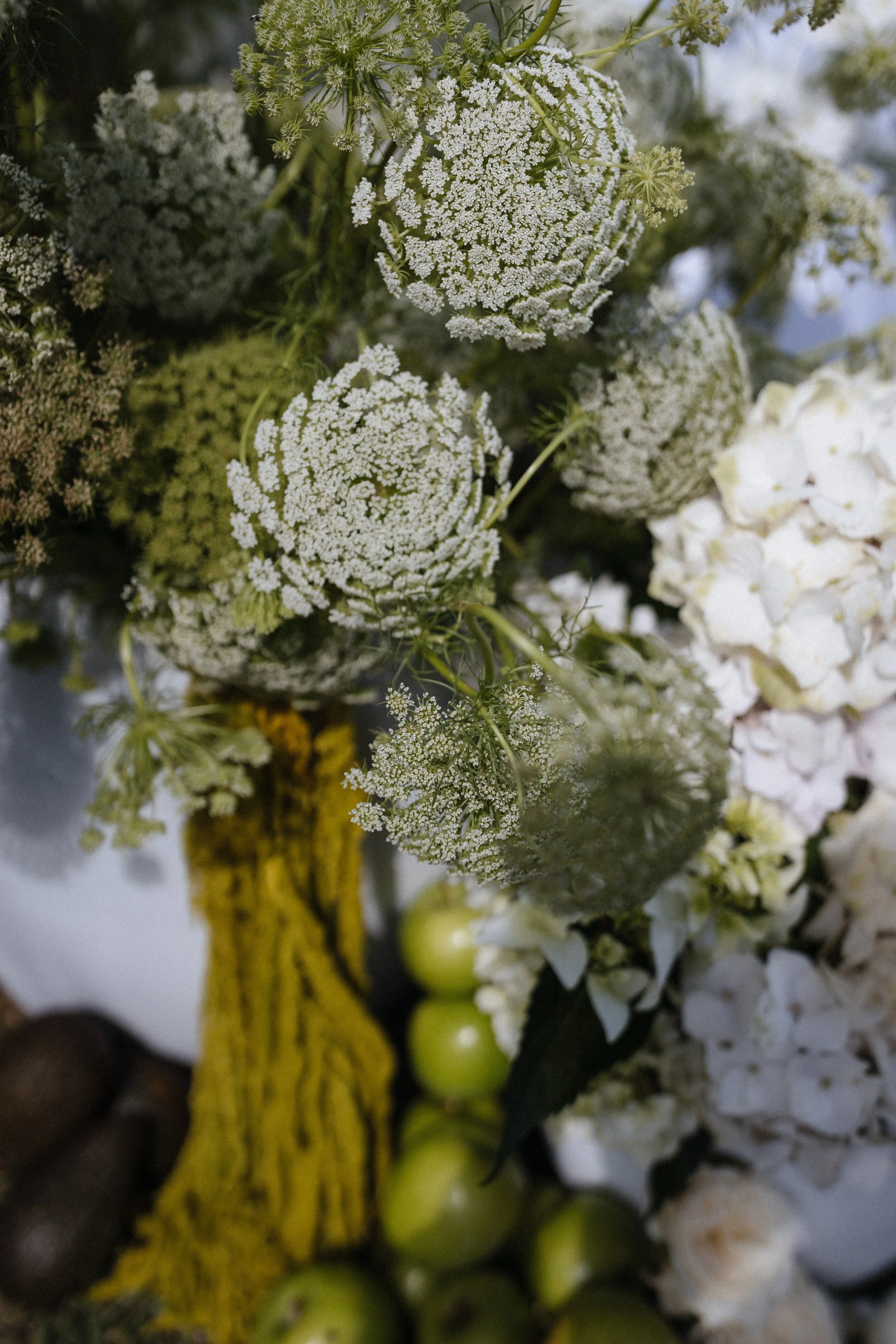 Close-up of a floral arrangement with white flowers, green grapes, and a yellow painted branch.