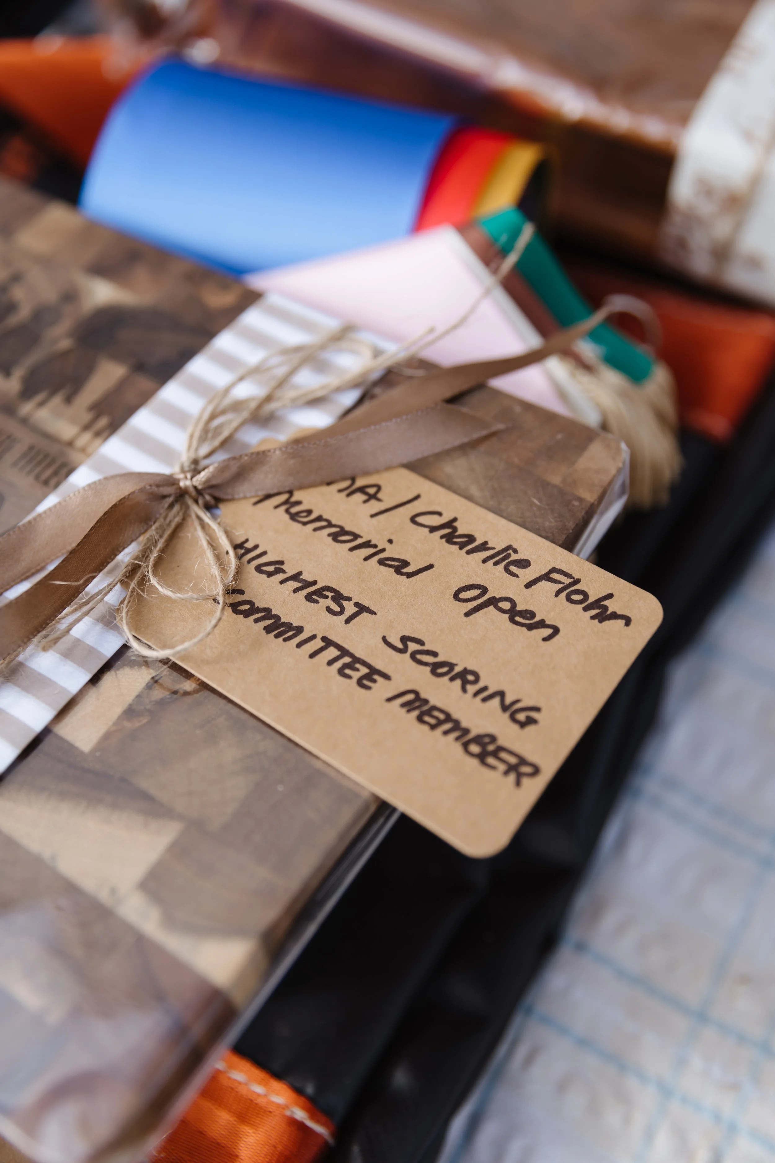 Close-up of a gift wrapped in brown paper with a handwritten note and tied with twine. The gift is placed on a wooden surface with other wrapped presents in the background.