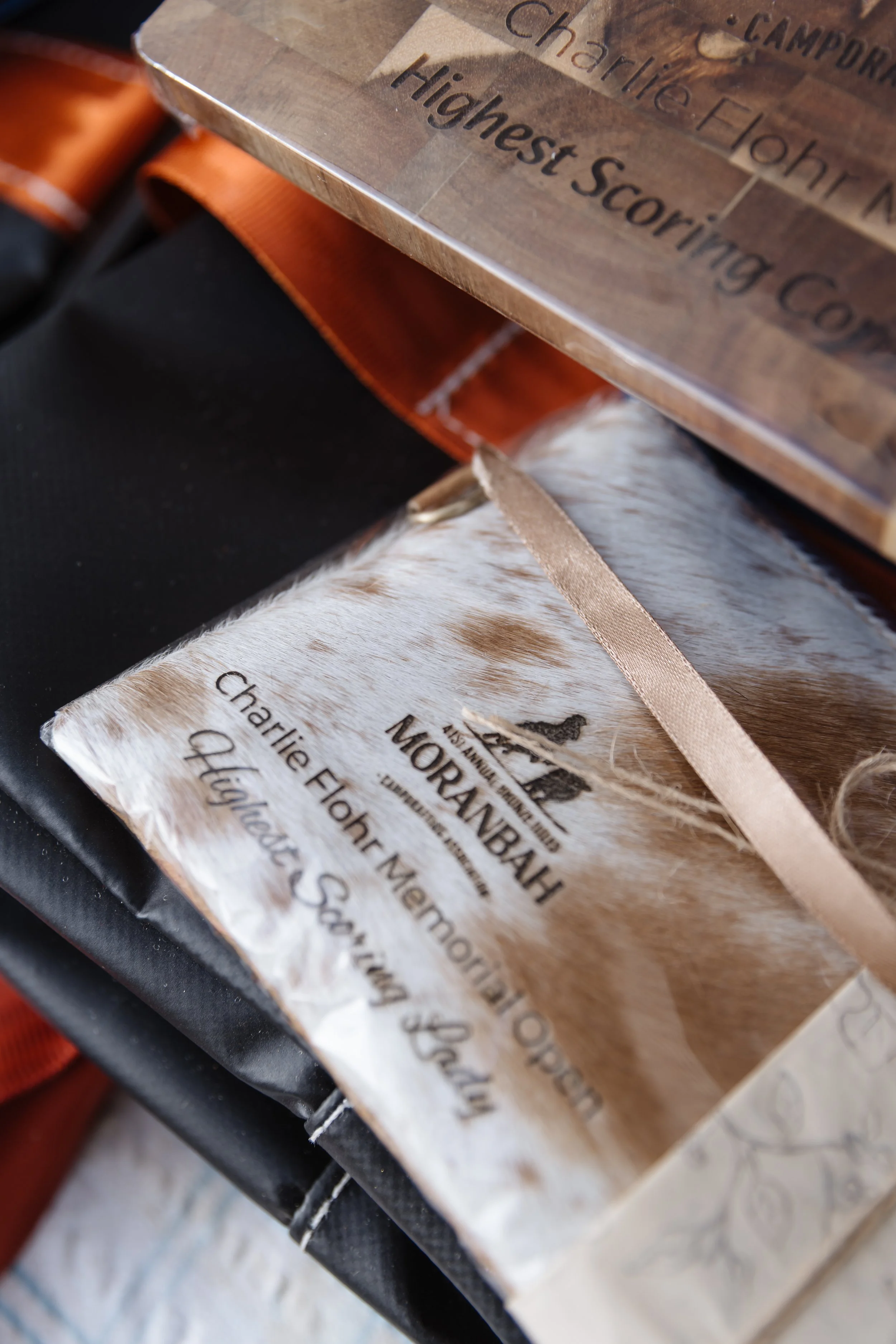 Close-up of a wooden plaque with engraved text, partly obscured, on an orange strap, with additional paper or fabric underneath.