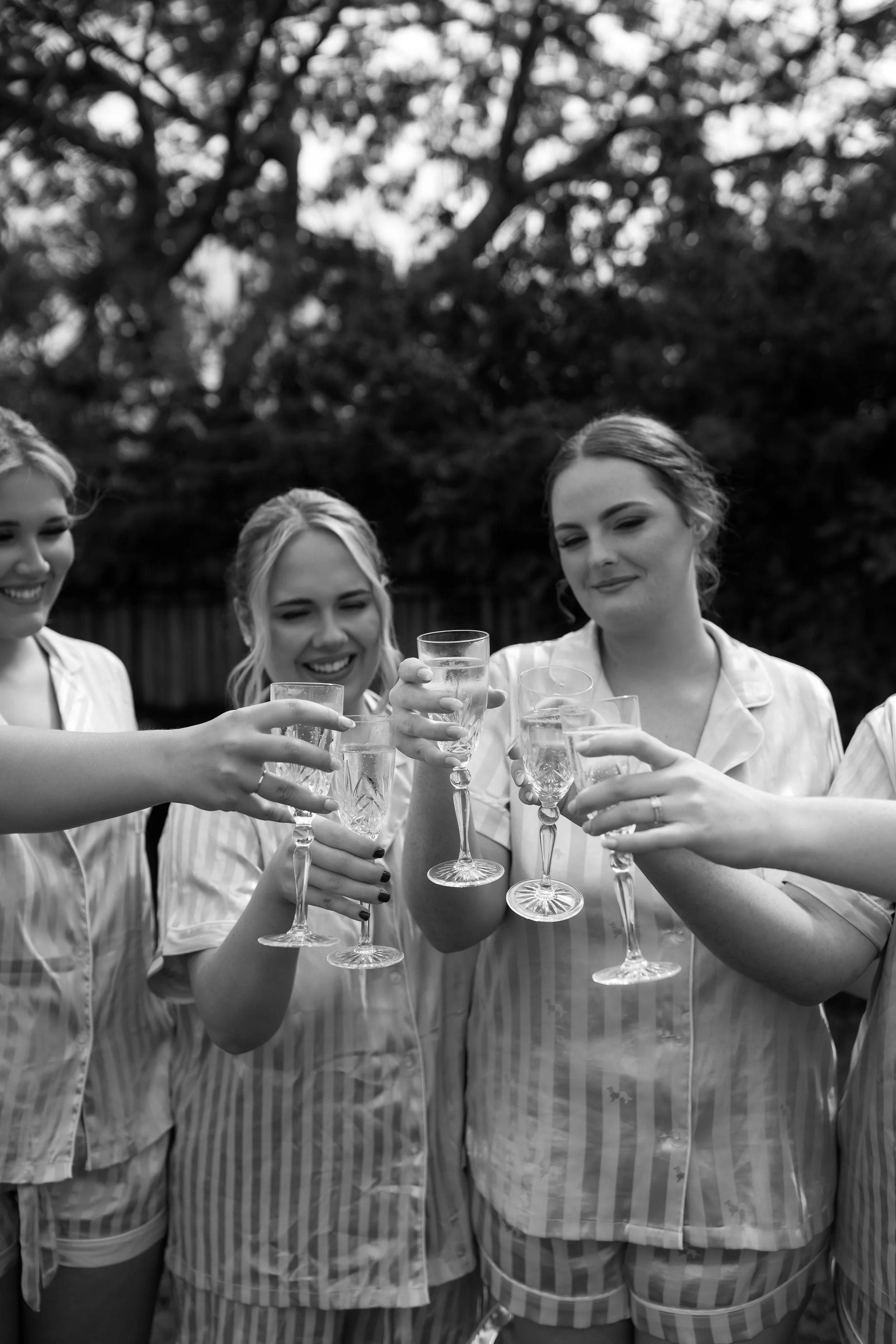 Four women in pajamas holding champagne glasses to make a toast outdoors.