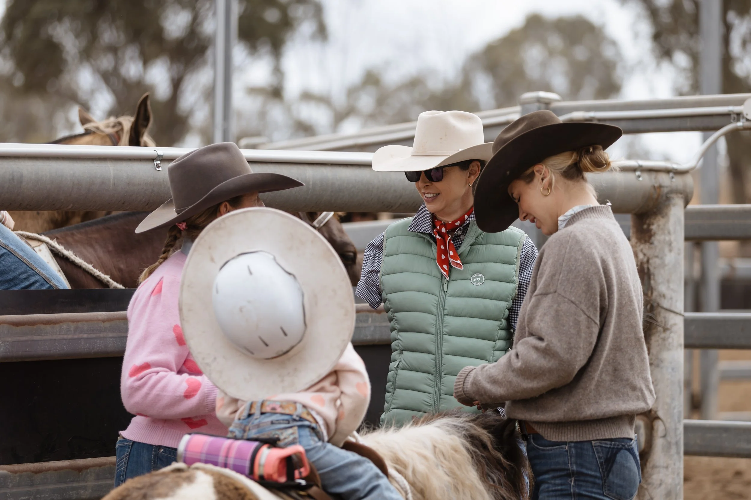 Group of people at a rodeo, wearing cowboy hats and standing near a livestock pen.
