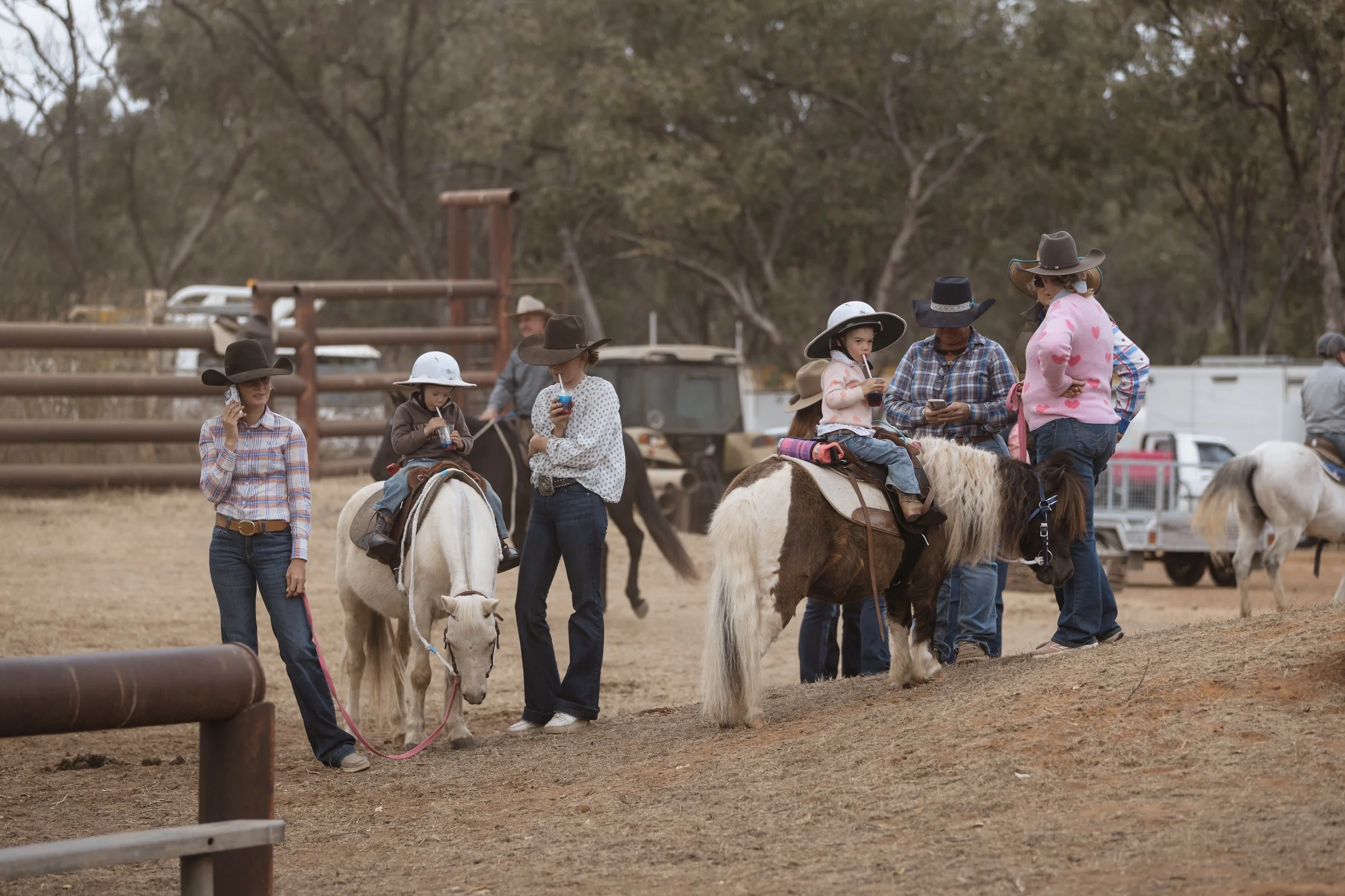 Group of children and adults wearing cowboy hats at a rodeo or country event, with some children riding ponies and others standing nearby.