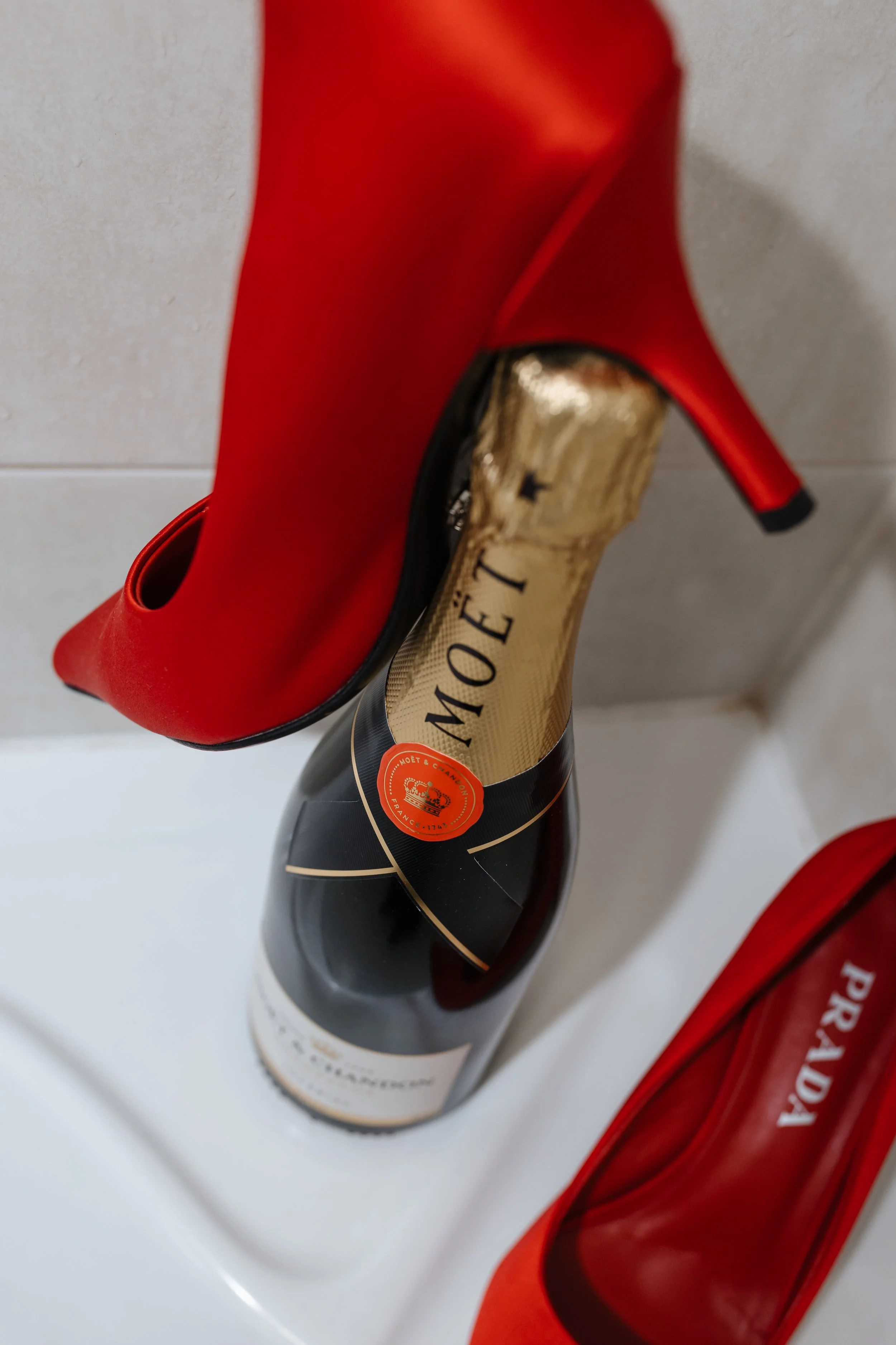 Red high-heeled shoe placed over a bottle of champagne and a red box.