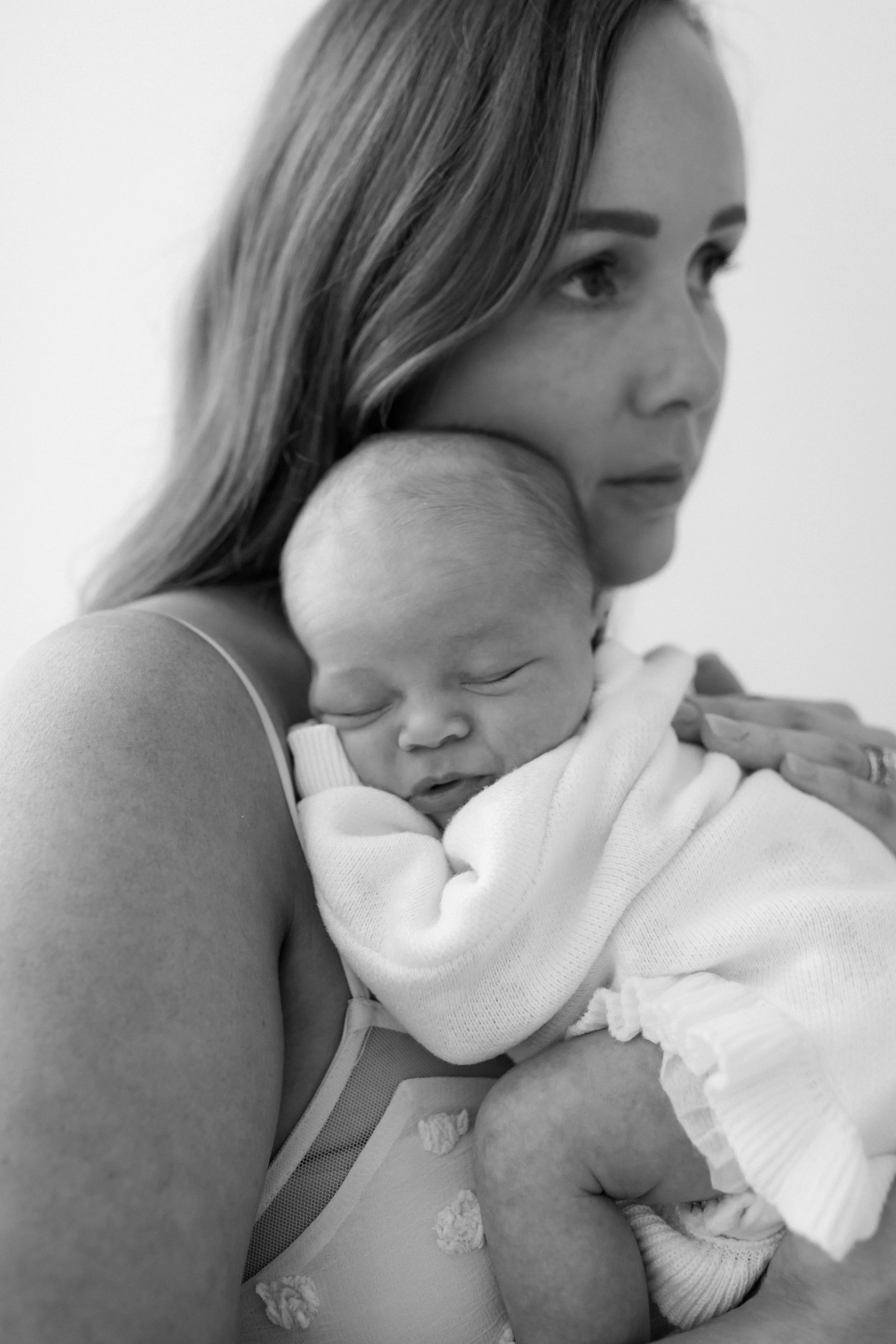 A woman holding a sleeping baby close to her chest, both with relaxed expressions; black-and-white photo