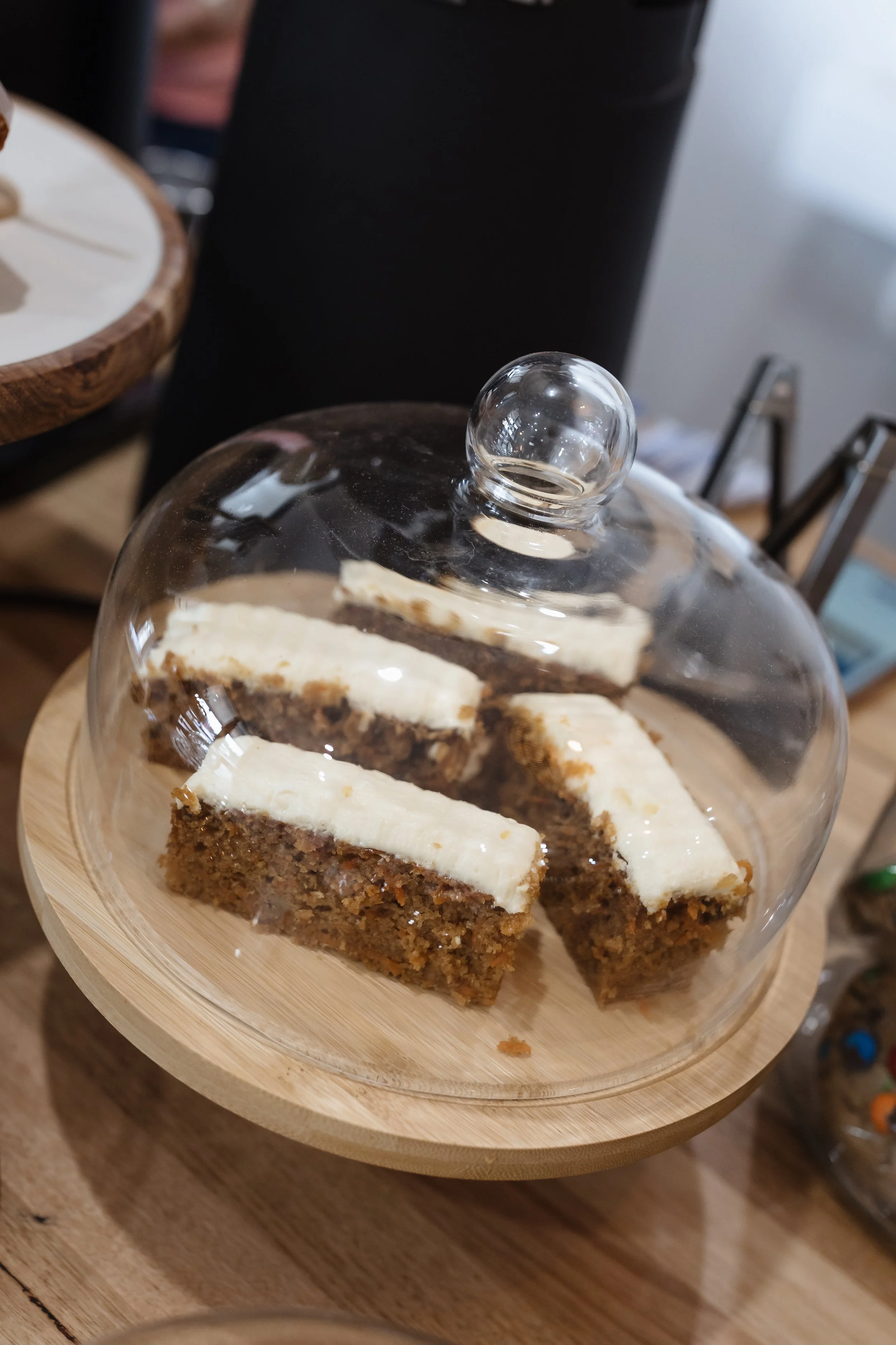 Slices of carrot cake with cream cheese frosting on a glass cake stand with a wooden base.