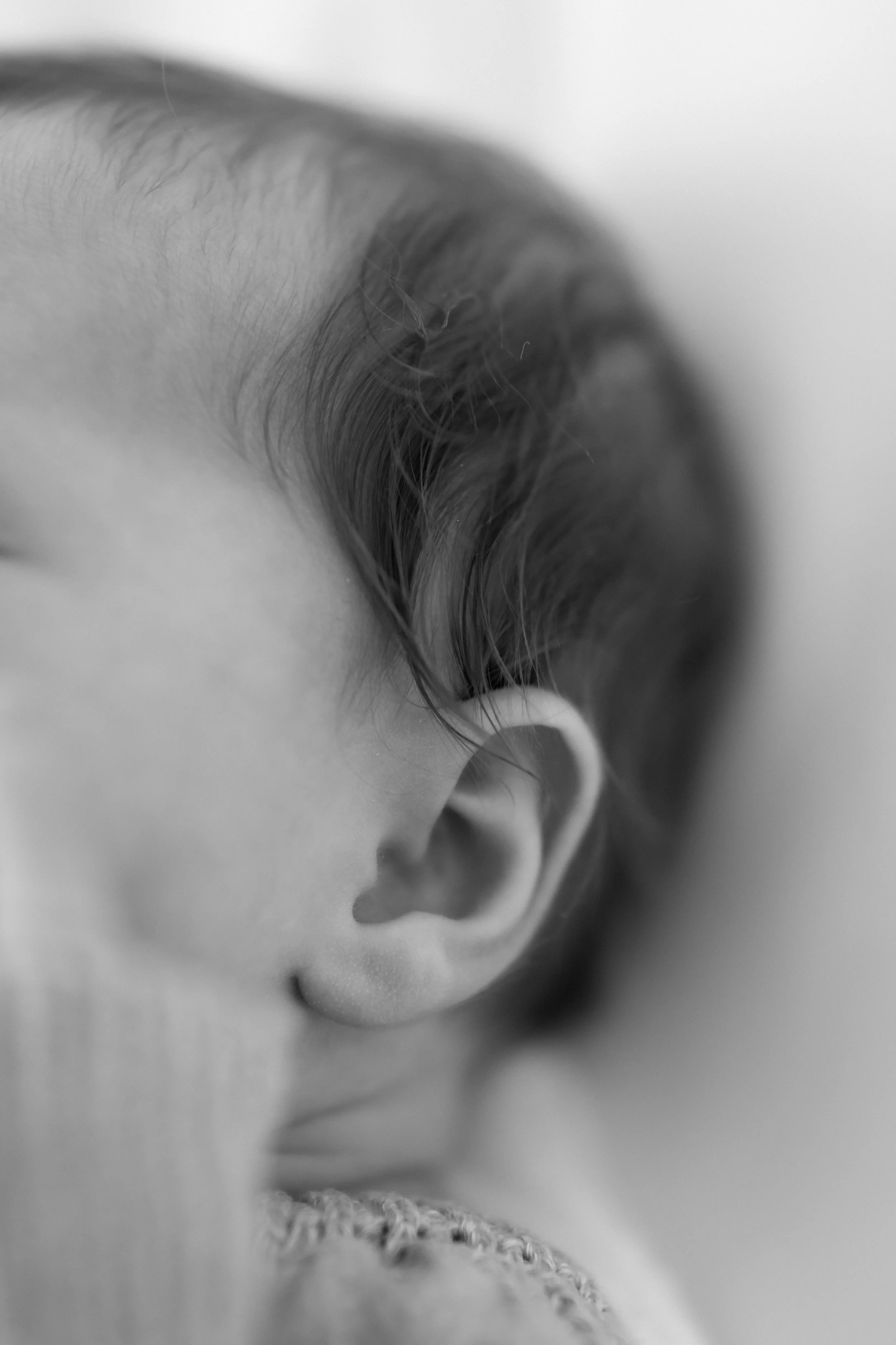 Close-up black and white photo of a child's ear and hair.