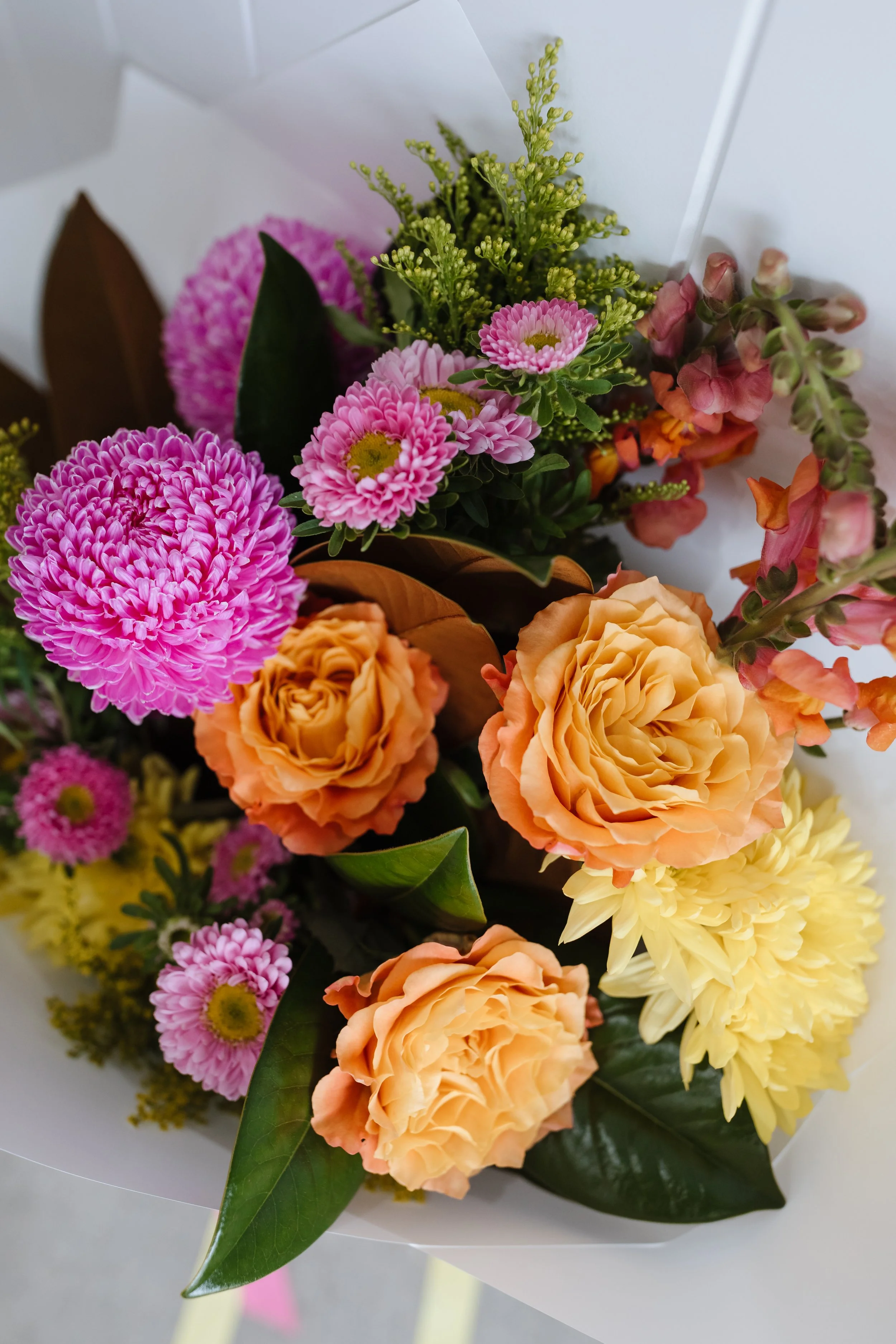 A bouquet of pink, orange, yellow, and green flowers wrapped in white paper.