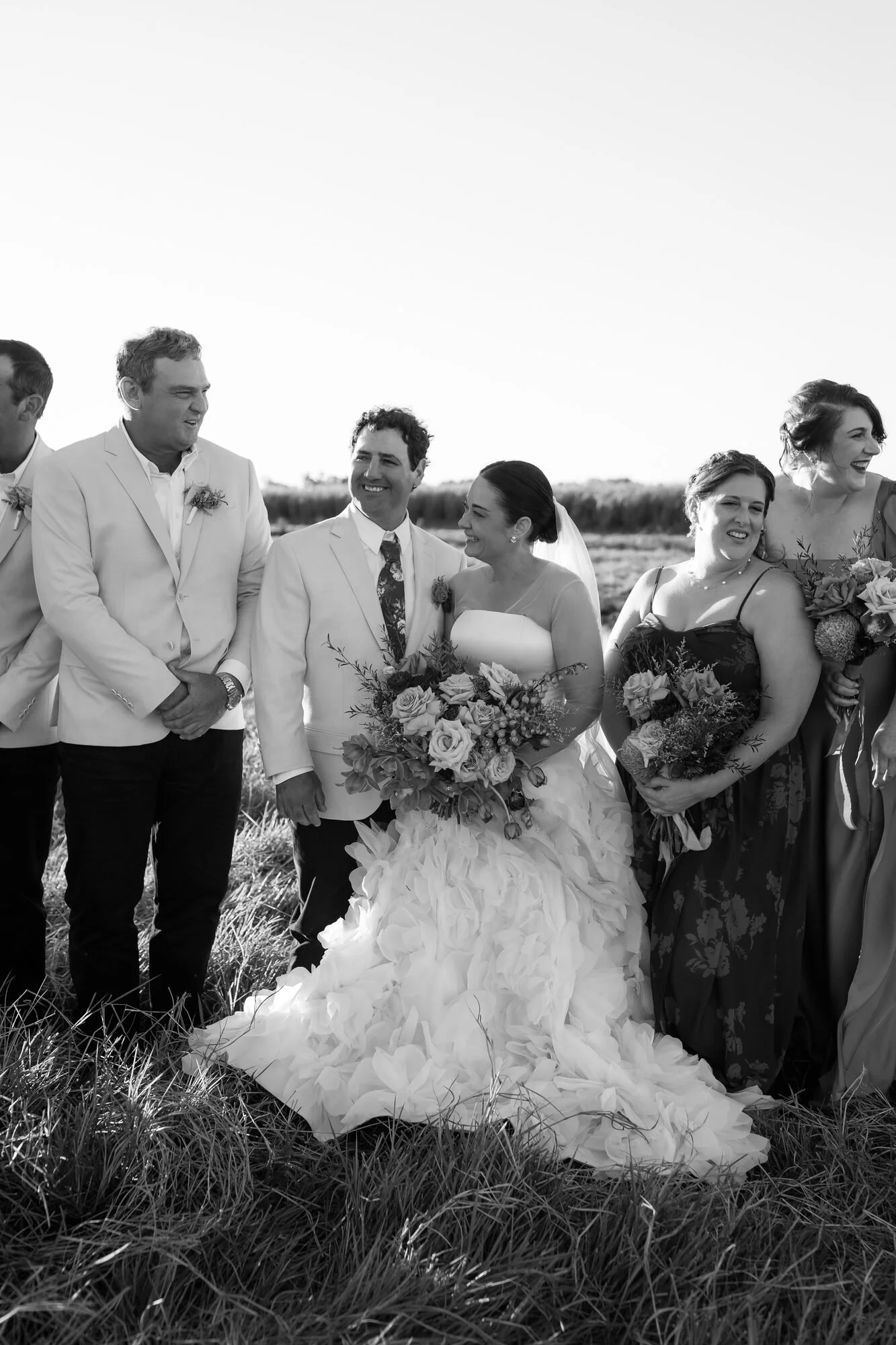 Black and white photo of a bride and groom standing outdoors with friends and family, celebrating their wedding.