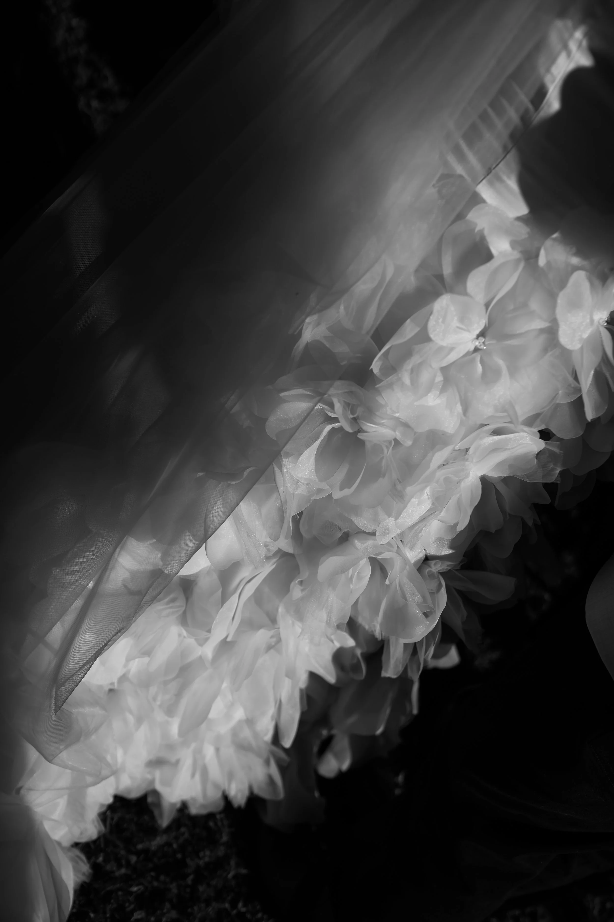 Black and white photo of floral arrangements with paper or fabric petals and leaves, with some draped fabric or veil nearby.