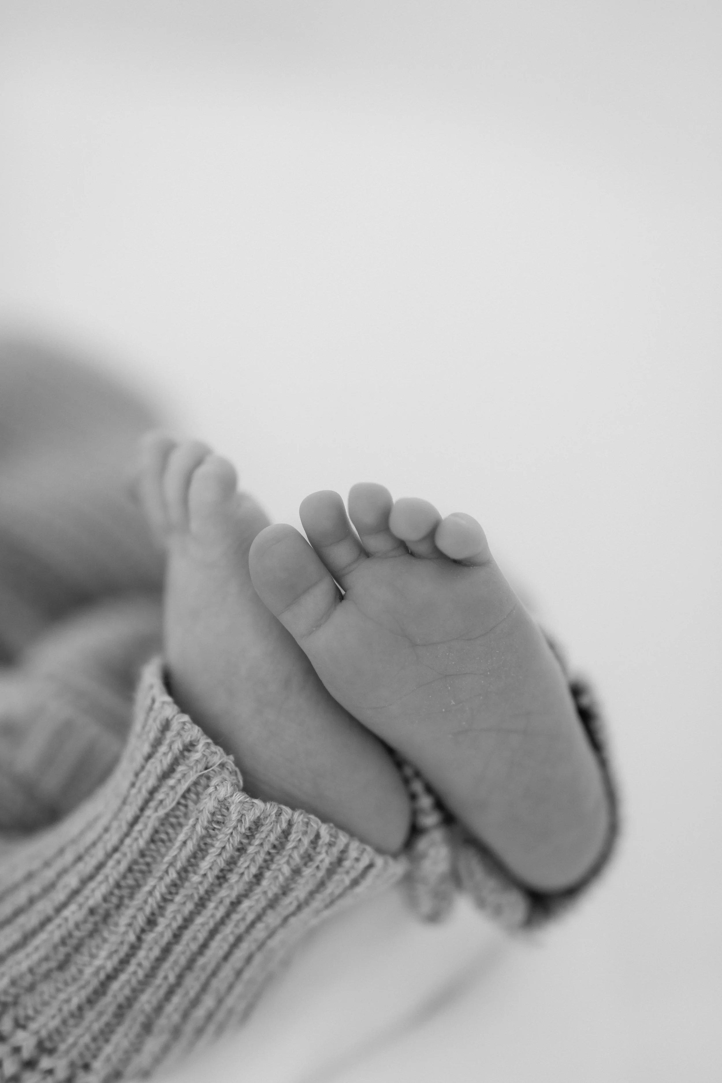 Close-up black and white photo of a baby's hand holding an adult's finger, with the baby wearing a striped knitted sleeve.