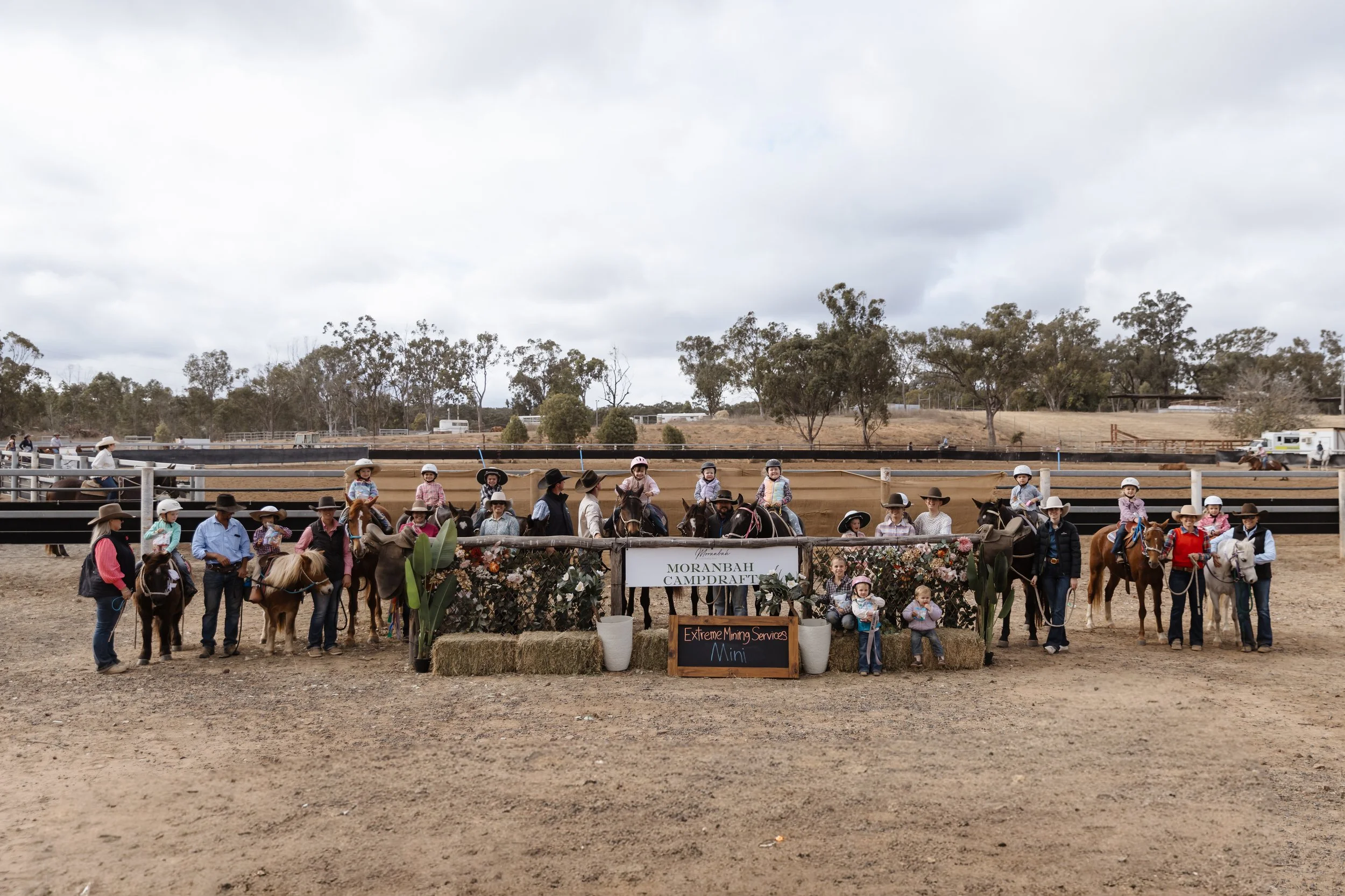 Group of children and adults on horseback at Morambah Campdraft event, with a cloudy sky and trees in the background.