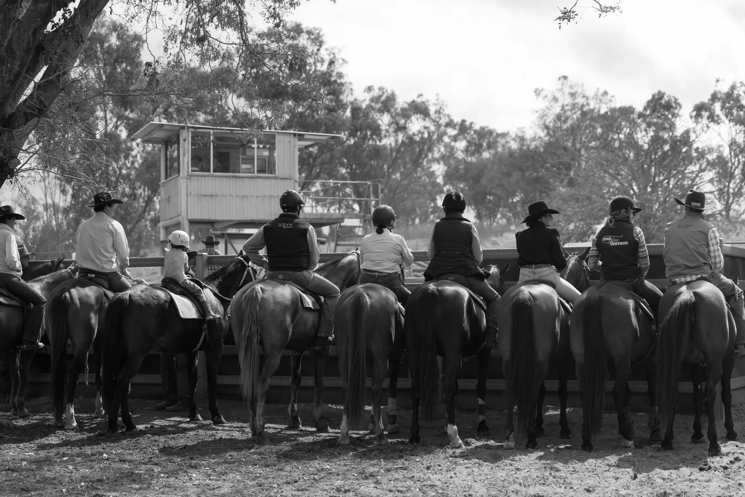A black and white photo of people riding horses at an equestrian event with a viewing platform in the background.