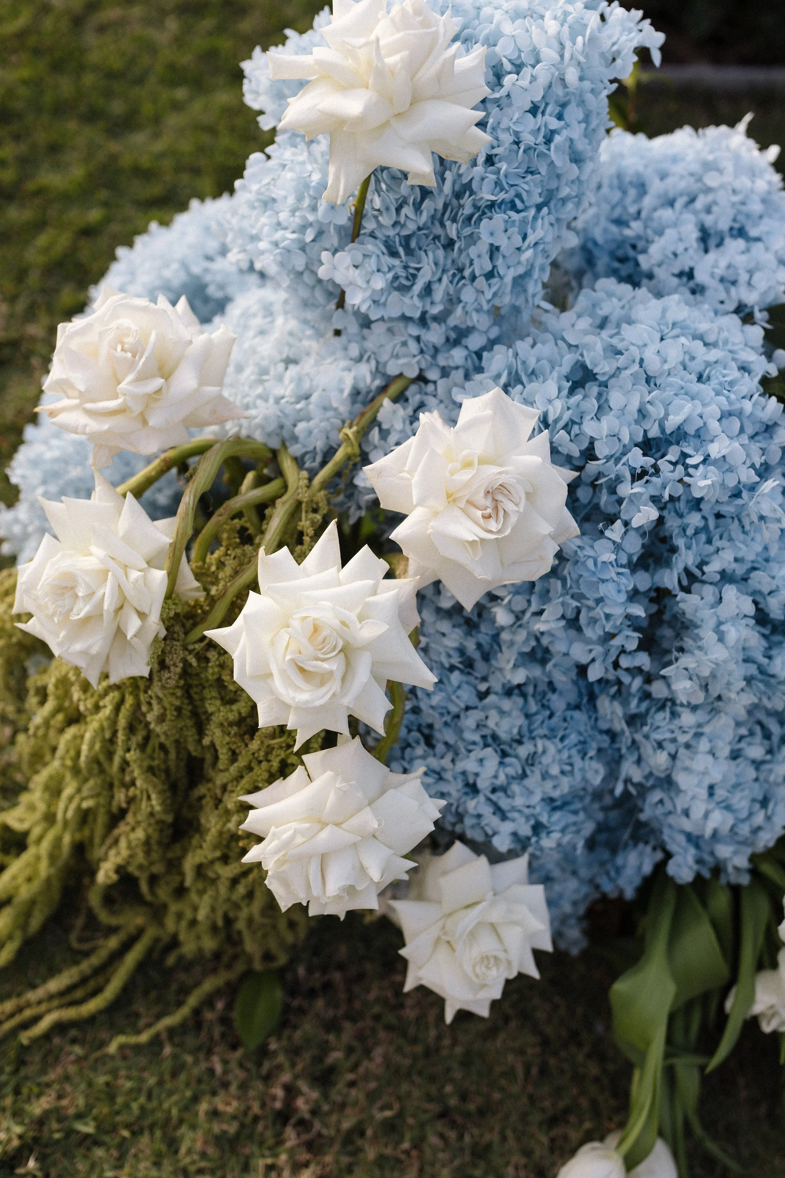 White roses and light blue hydrangeas arranged together on green grass.