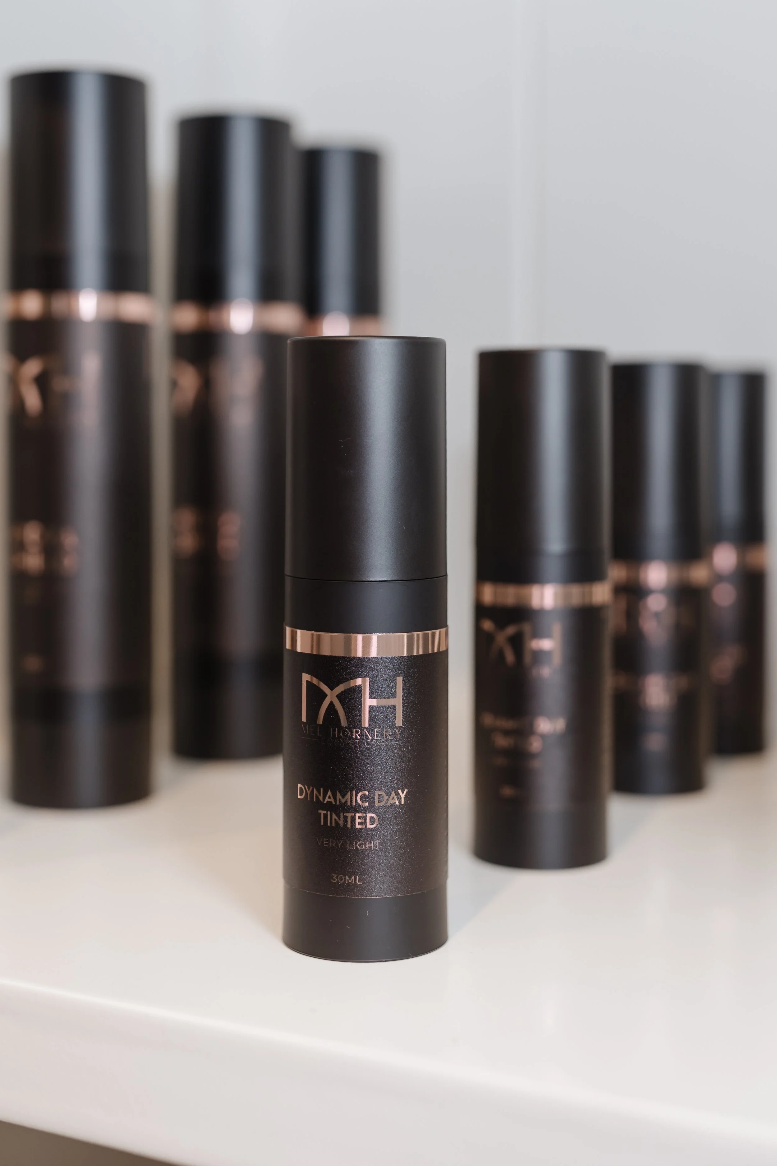 A row of black cylindrical bottles labeled 'DYNAMIC DAY TINTED Very Light' standing on a white surface with a white wall background.