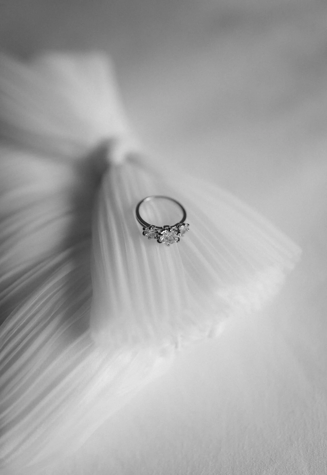 A silver ring with a large central gemstone surrounded by smaller stones, resting on a white surface with shadows and folds.
