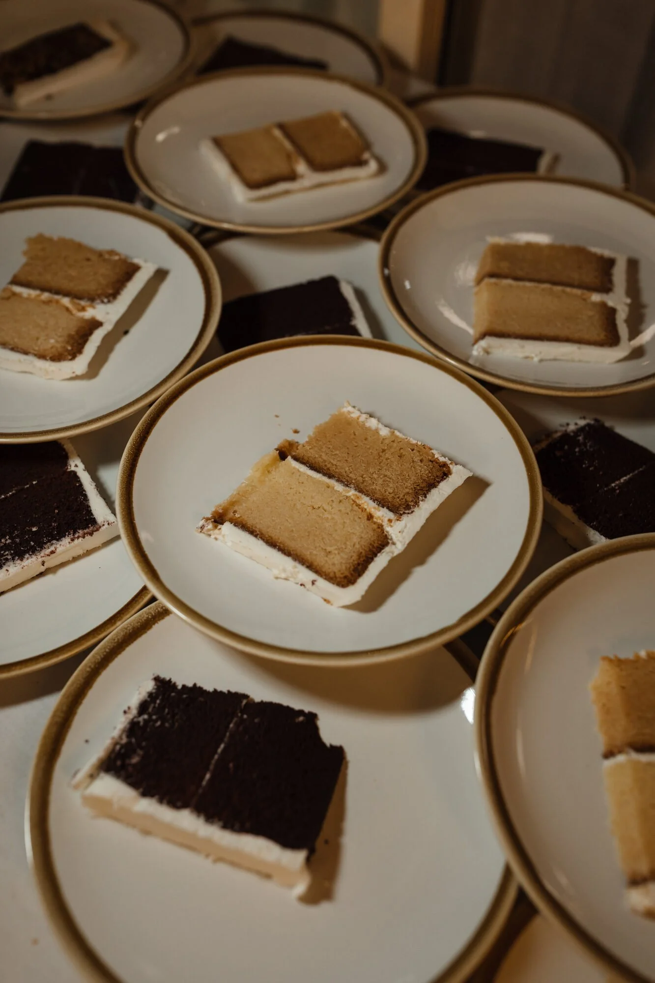 Multiple plates with sliced cake, some with chocolate frosting and others with vanilla and caramel layers.