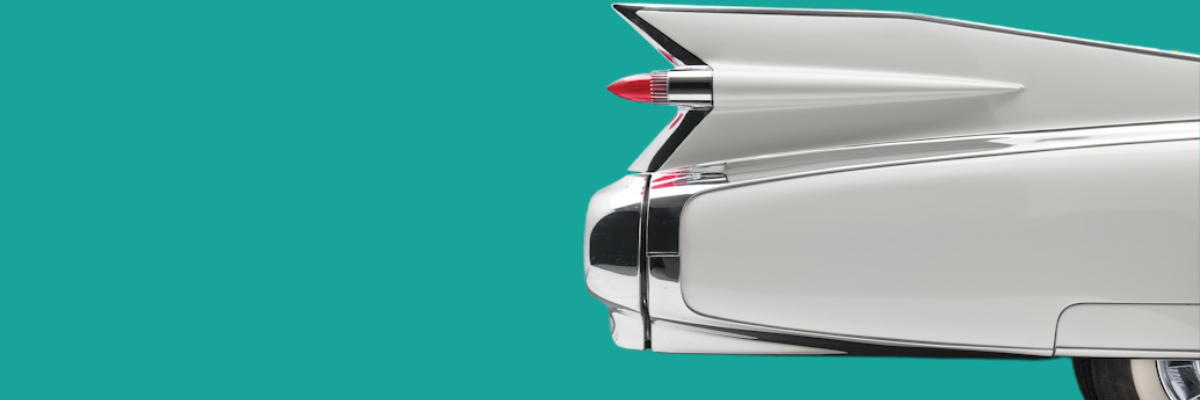 Close-up of the rear end of a vintage white Cadillac with a red lipstick-shaped hairbrush in the open trunk.