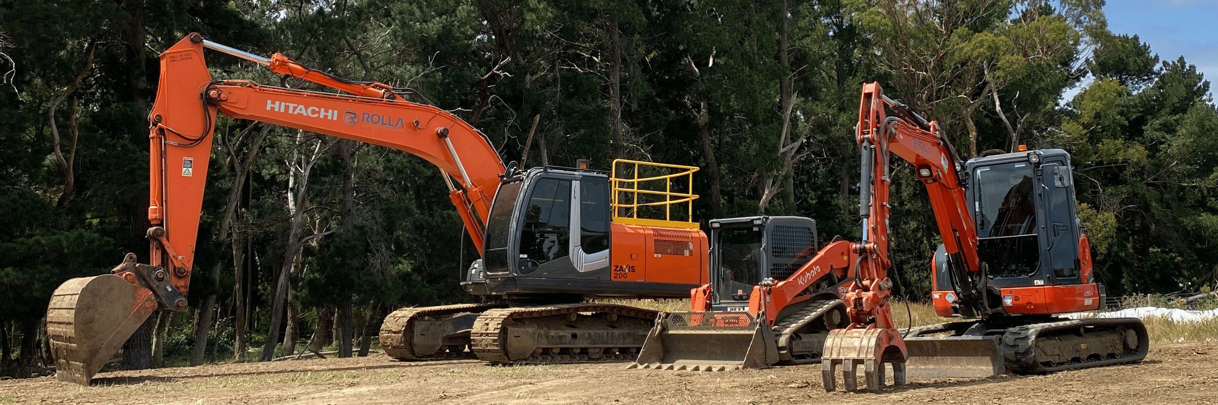 One orange excavator with track wheels is parked next to a small orange bulldozer on a recently prepared site of flat brown earth.