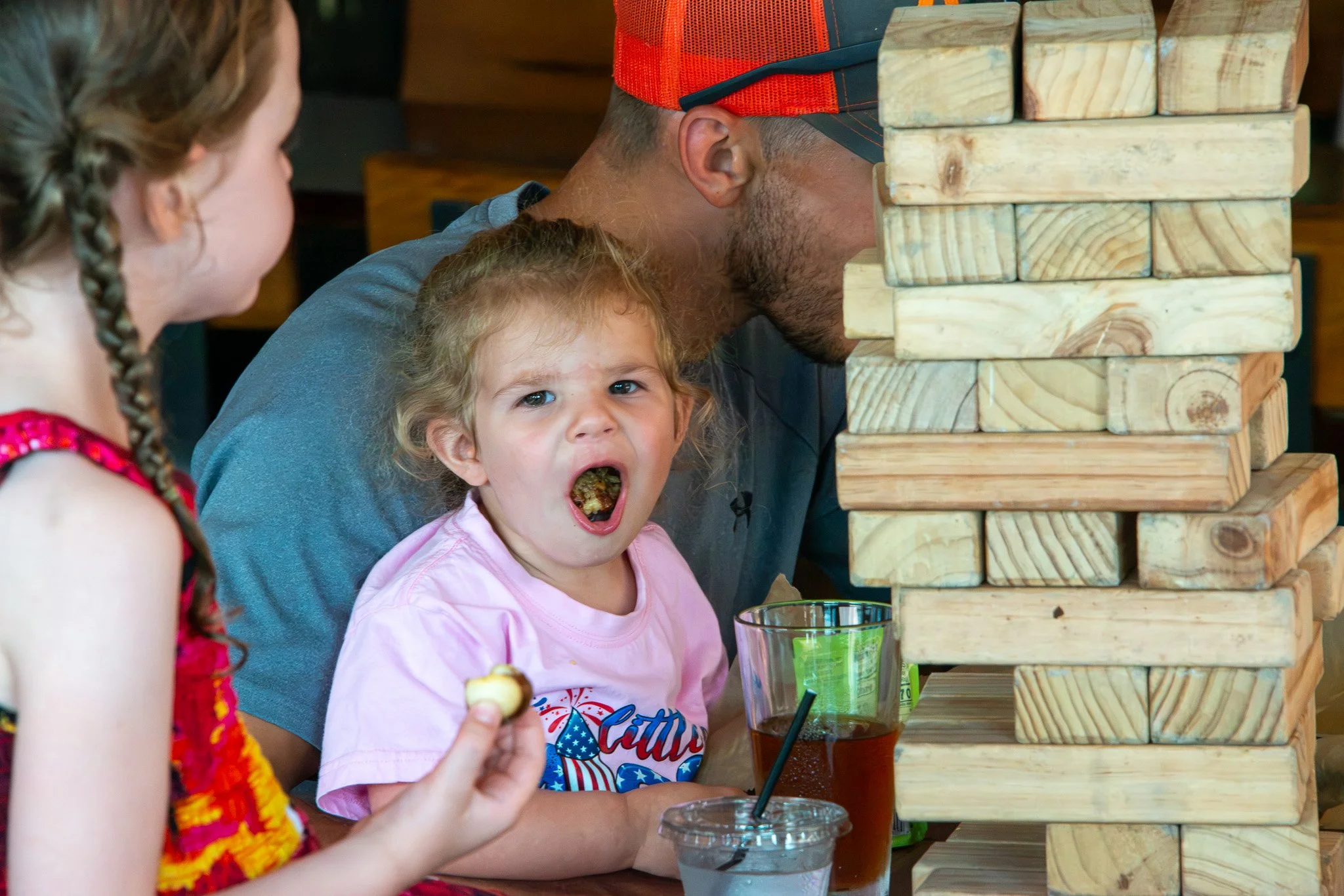 Children and an adult playing a giant Jenga game at a restaurant or cafe.
