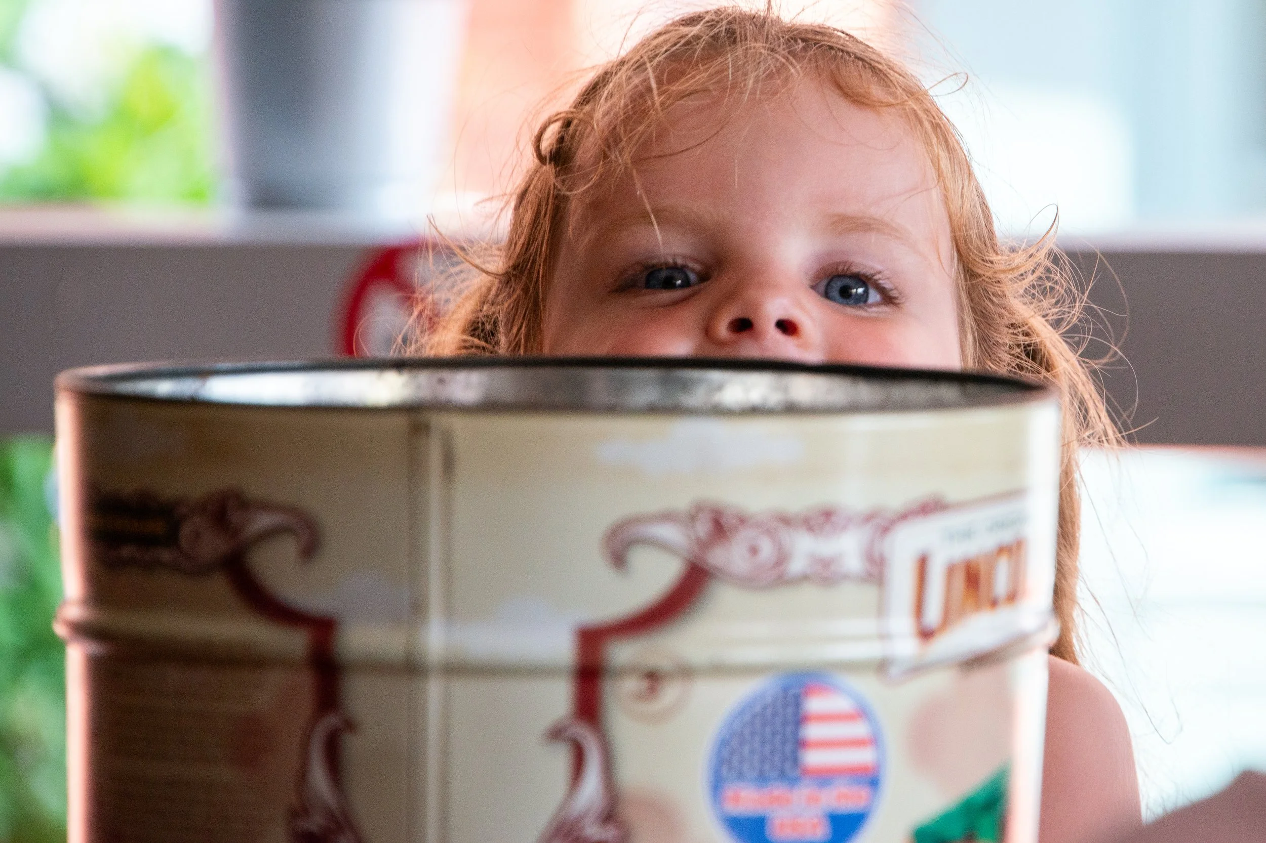 A young girl with red hair peeking over a container with a blue and red label, possibly ice cream or frozen dessert.