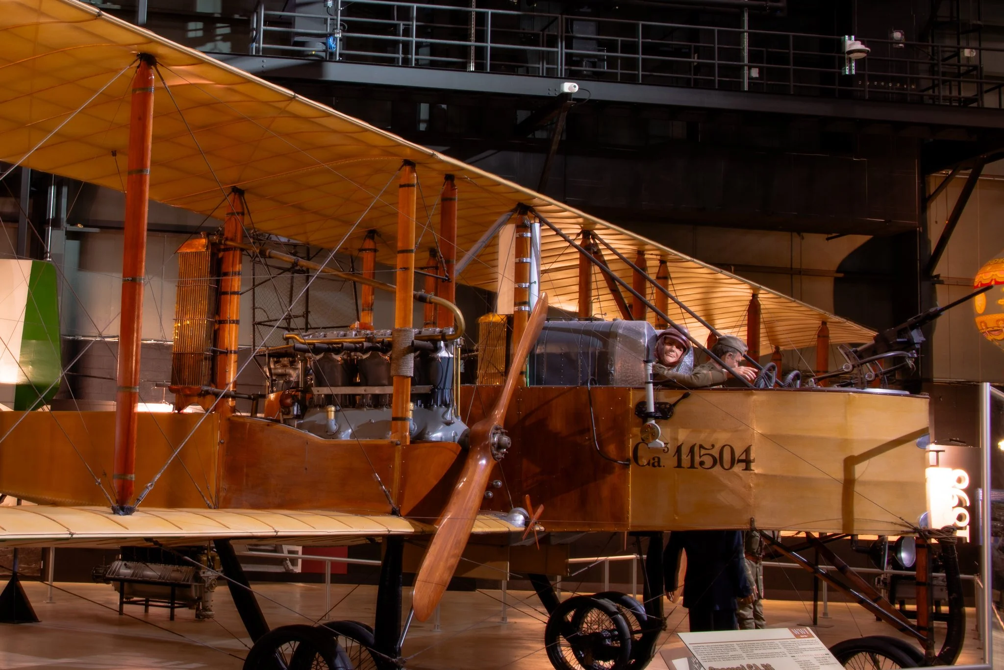 A vintage airplane with a wooden body and large yellow fabric wings on display. The aircraft has two people sitting in the cockpit, and it is labeled with Guinness Book of World Records and the number Ca. 11504.