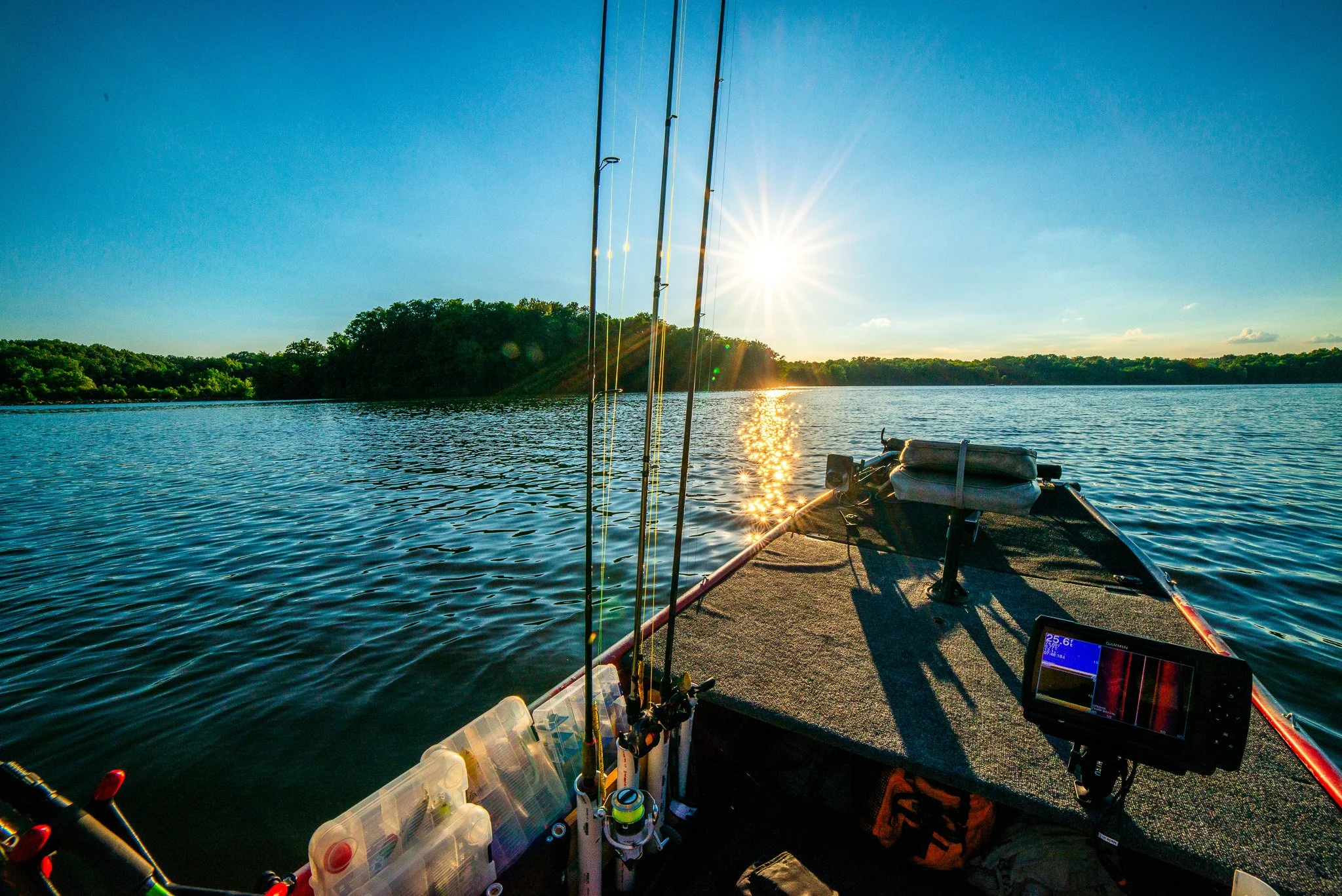 Fishing boat at sunset on a calm river with fishing rods and equipment on deck.