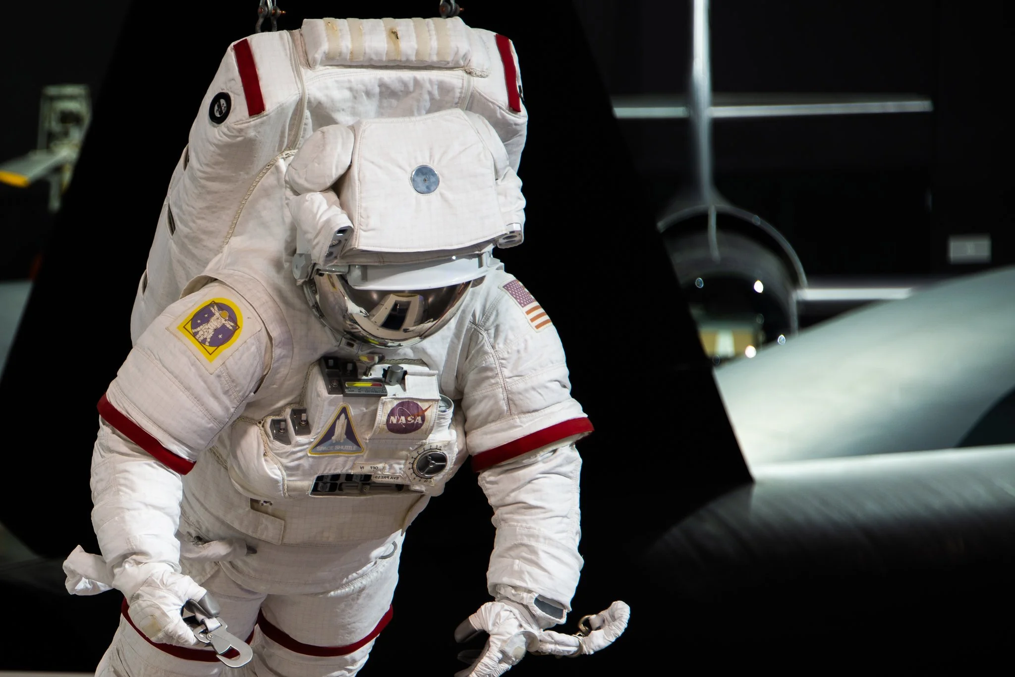 Astronaut in a white spacesuit with NASA patches, standing in space next to a spacecraft, with the Earth visible in the background.