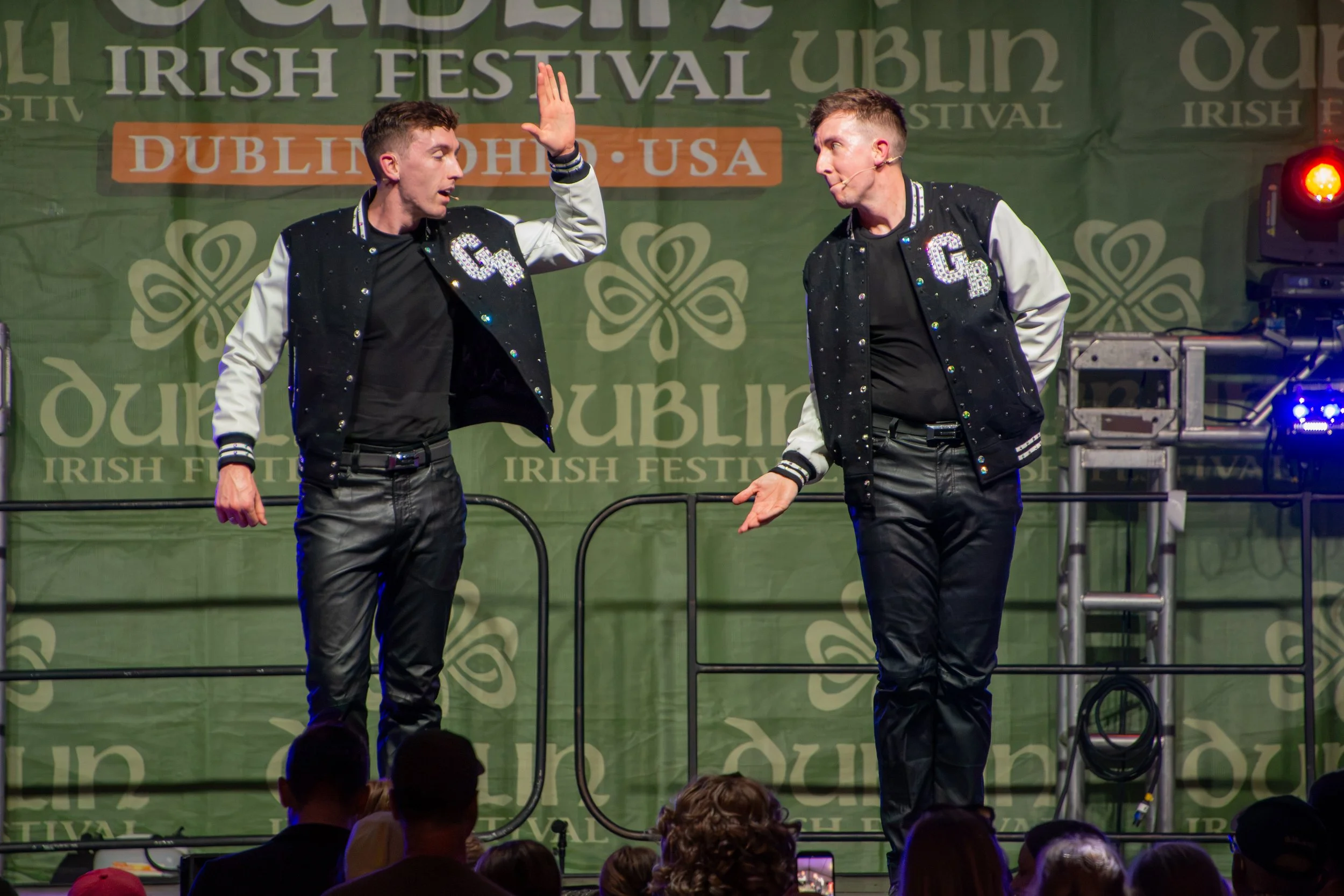Two performers on stage at the Dublin Irish Festival engaging in a lively act; background banner with festival information; audience visible in foreground.