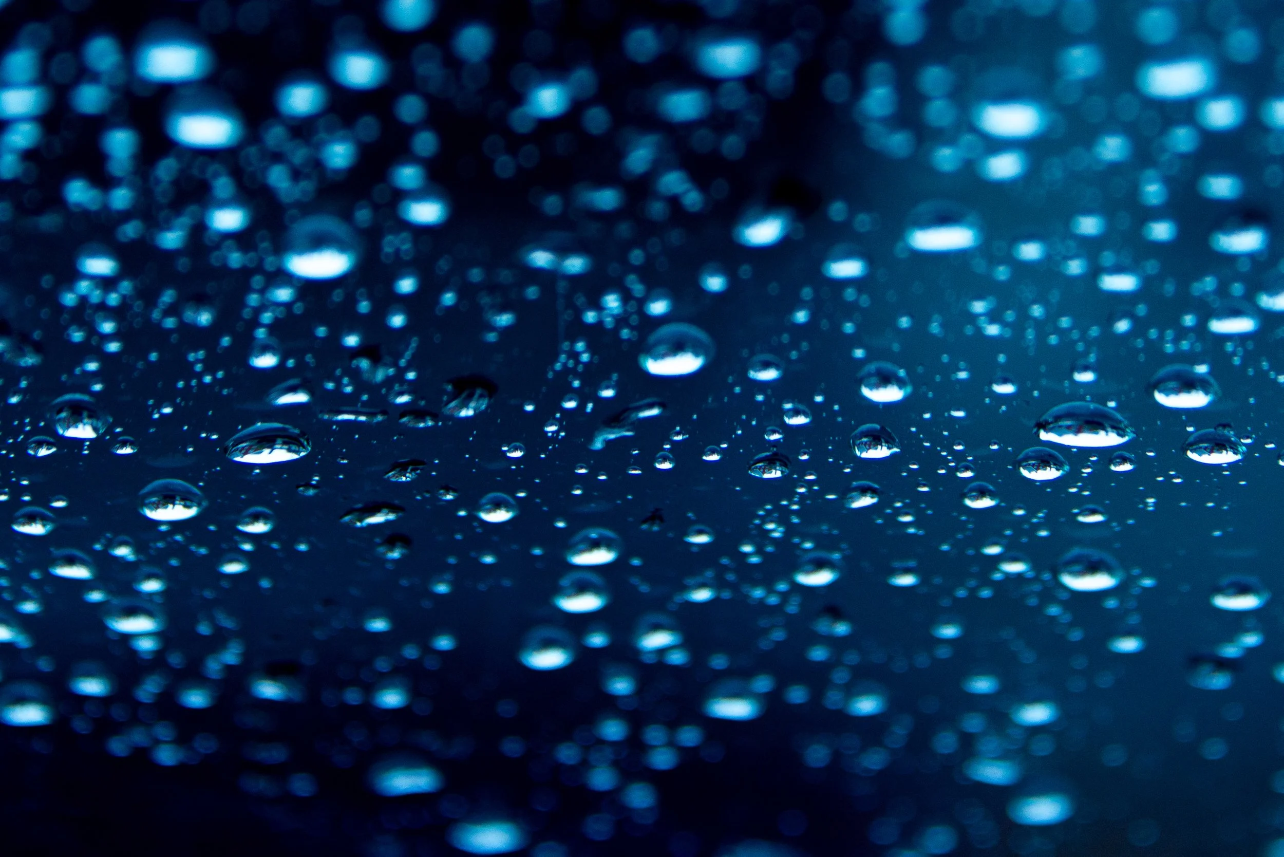 Close-up of water droplets on a surface, reflecting blue light, creating a bokeh effect with blurred blue circles in the background.