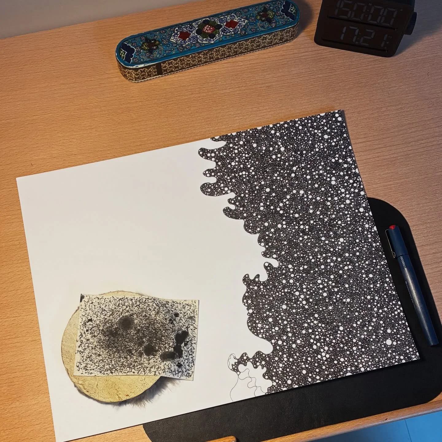 Overhead studio scene documenting process art by Abdushakur, featuring a developing monochrome ink field on board, a traditional decorative pen case, and a session timer.