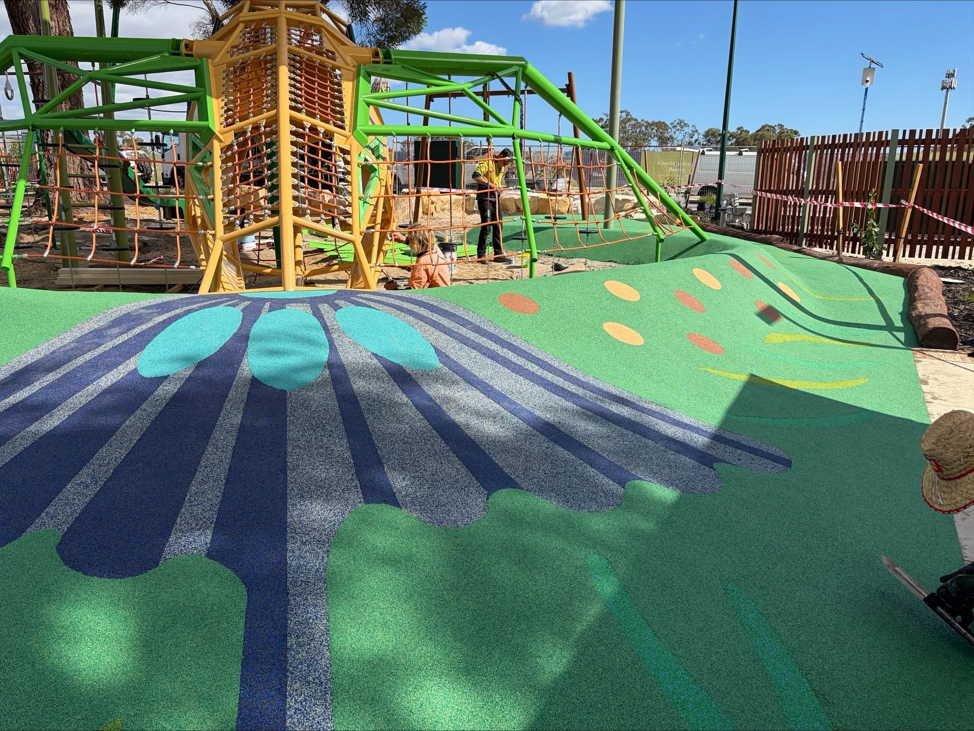 Colorful playground with climbing structure, soft ground, and a butterfly design on the ground.