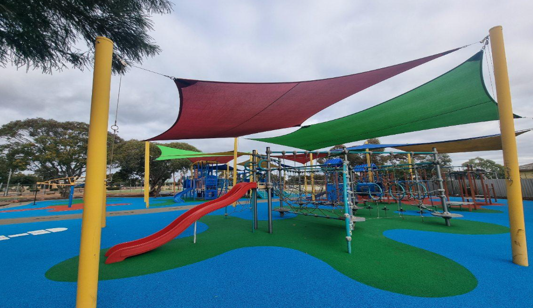 Colorful playground with slides, climbing structures, and shade sails in a park.