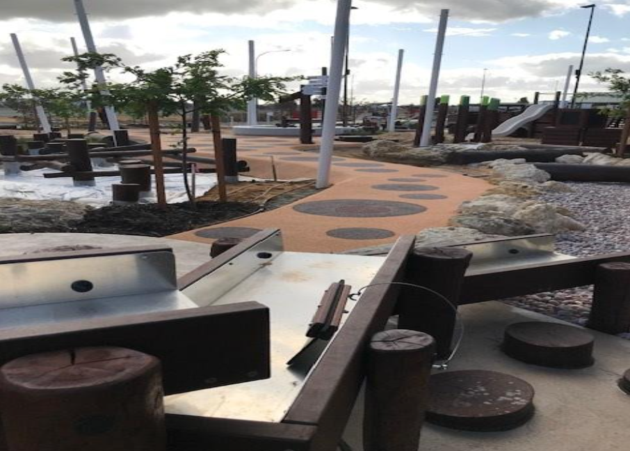 Outdoor playground area with a mini golf course, rocks, small trees, and a winding path, under a cloudy sky.