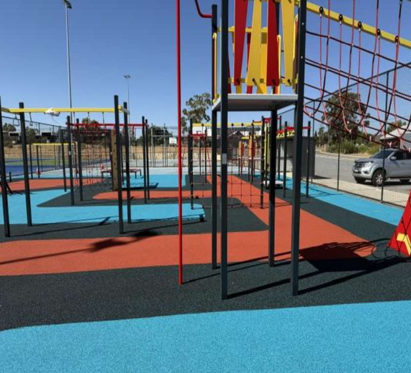 Colorful playground with climbing structures, ropes, and slides on a rubberized ground.