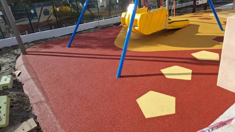 Colorful playground with a red rubberized surface, yellow hexagonal stepping stones, and a yellow swing set with blue support poles.