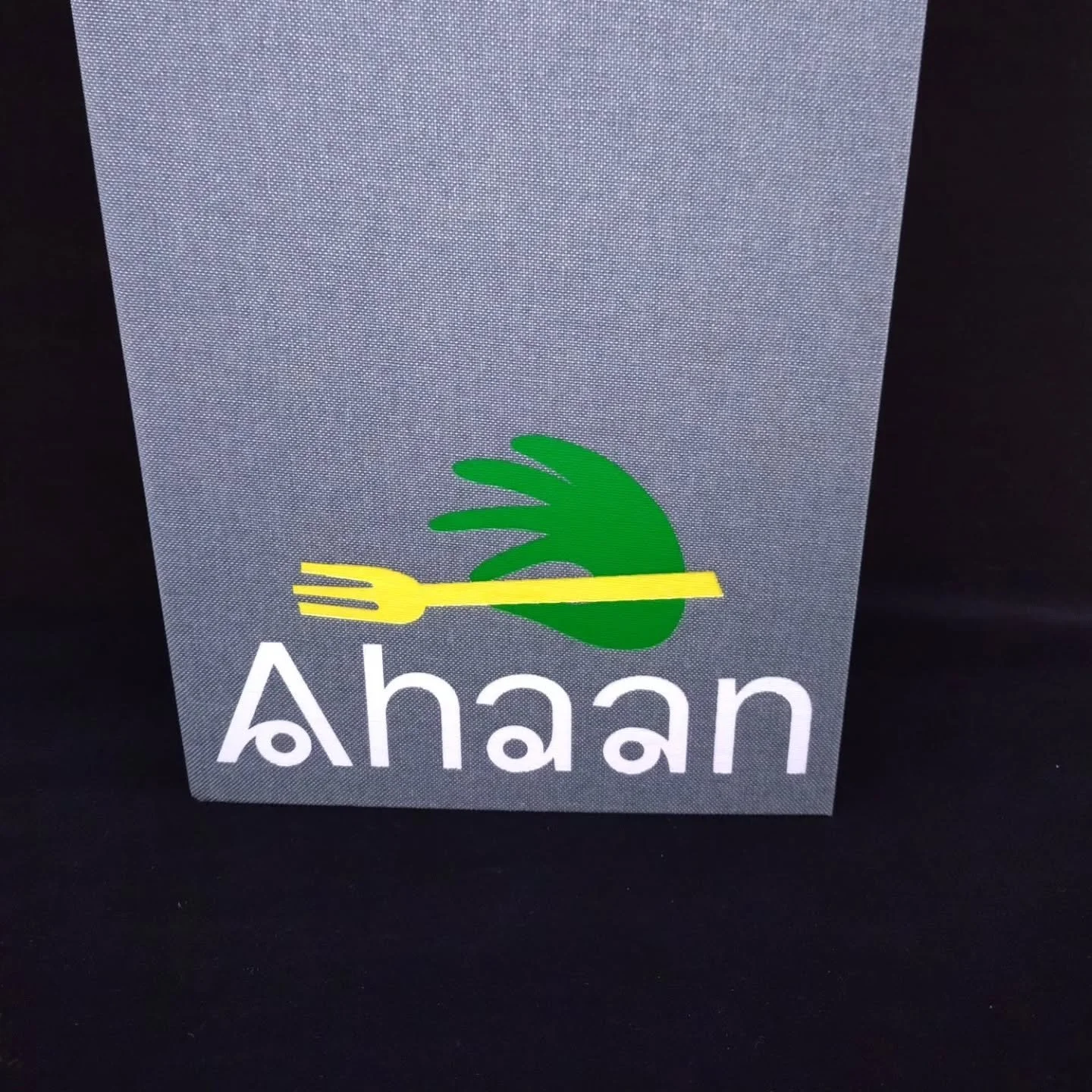 Logo med en grønn finger som holder en gaffel i gult, og tekst som sier 'Ahaan'.
