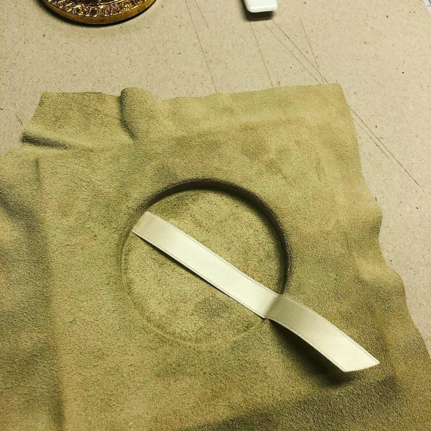 Et stykke beige stoff med en sirkel utklippet i midten, en hvit rutete bånd og noe som ligner på et målebånd liggende på stoffet.