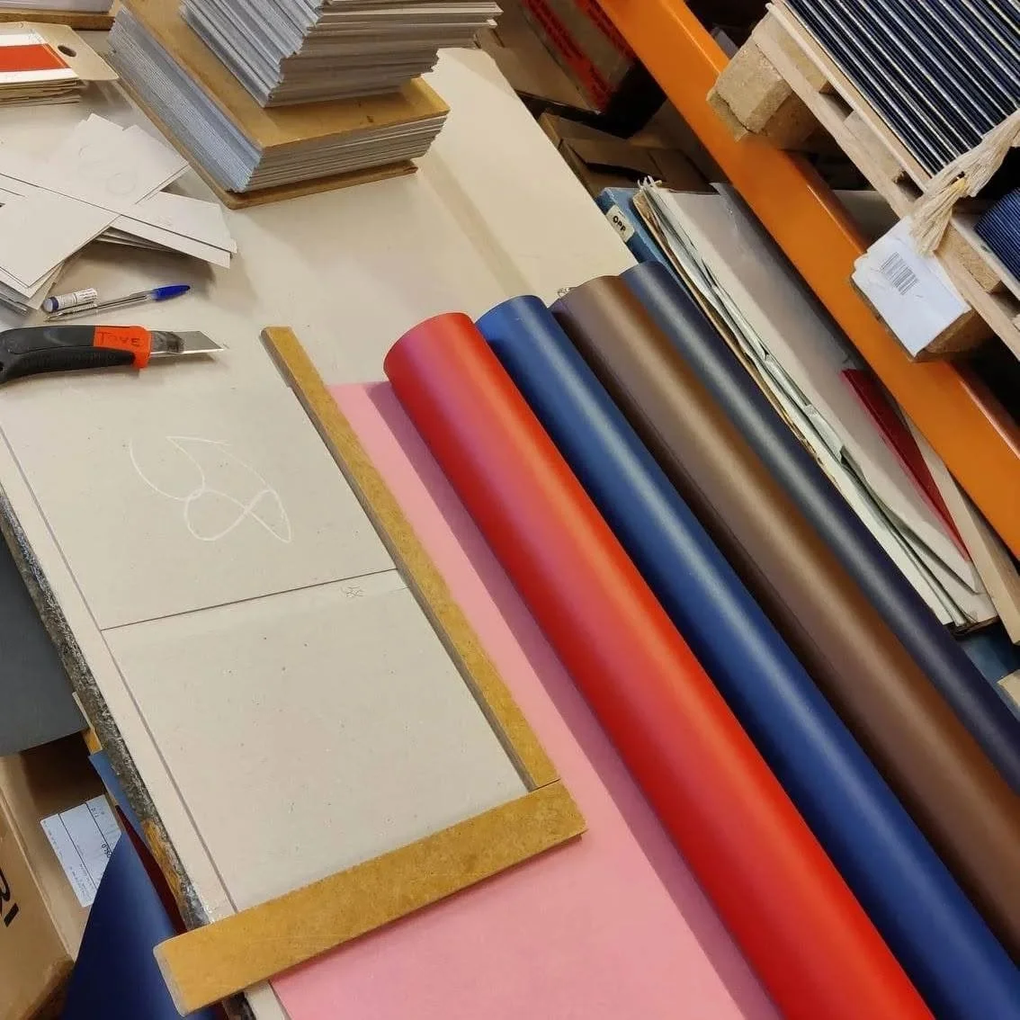 Arbeidsbord med fargekart av vinyl, papirer, verktøy og materialer for dekorasjon eller produksjon.