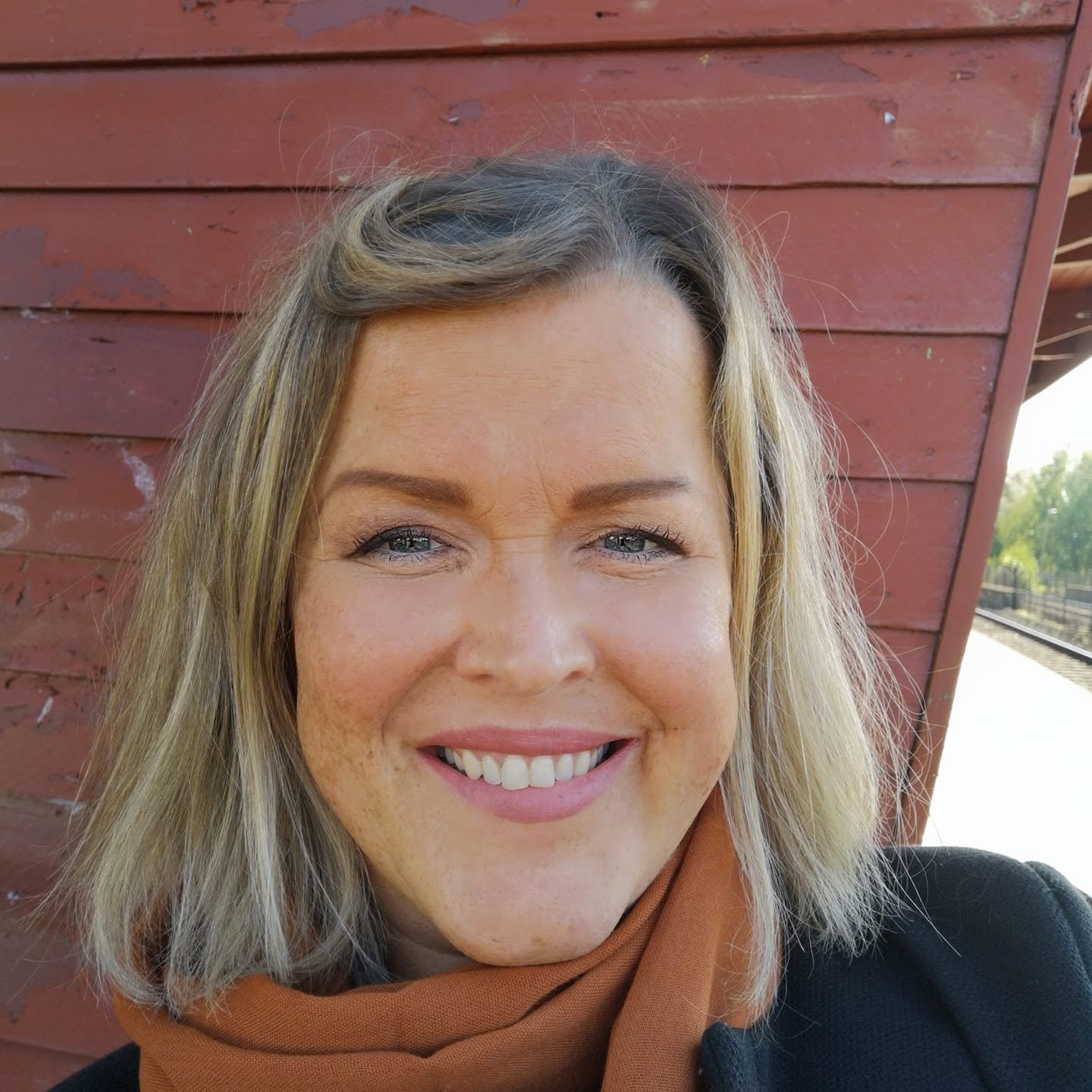 Nærbilde av en smilende kvinne med blondt hår foran en rød vegg.