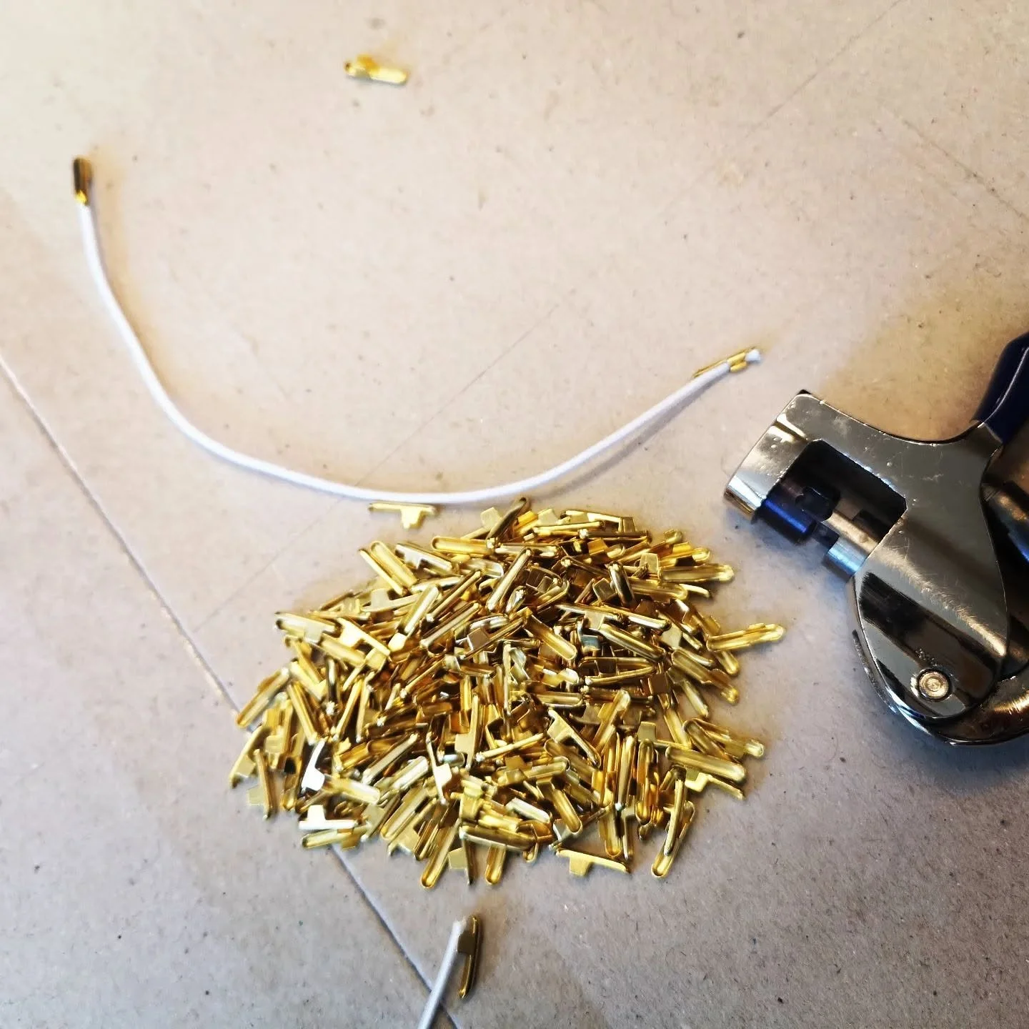 En bunke med små gullfargede metallkomponenter, en varmepistol og en hvit tråd med små gullfargede deler festet på.