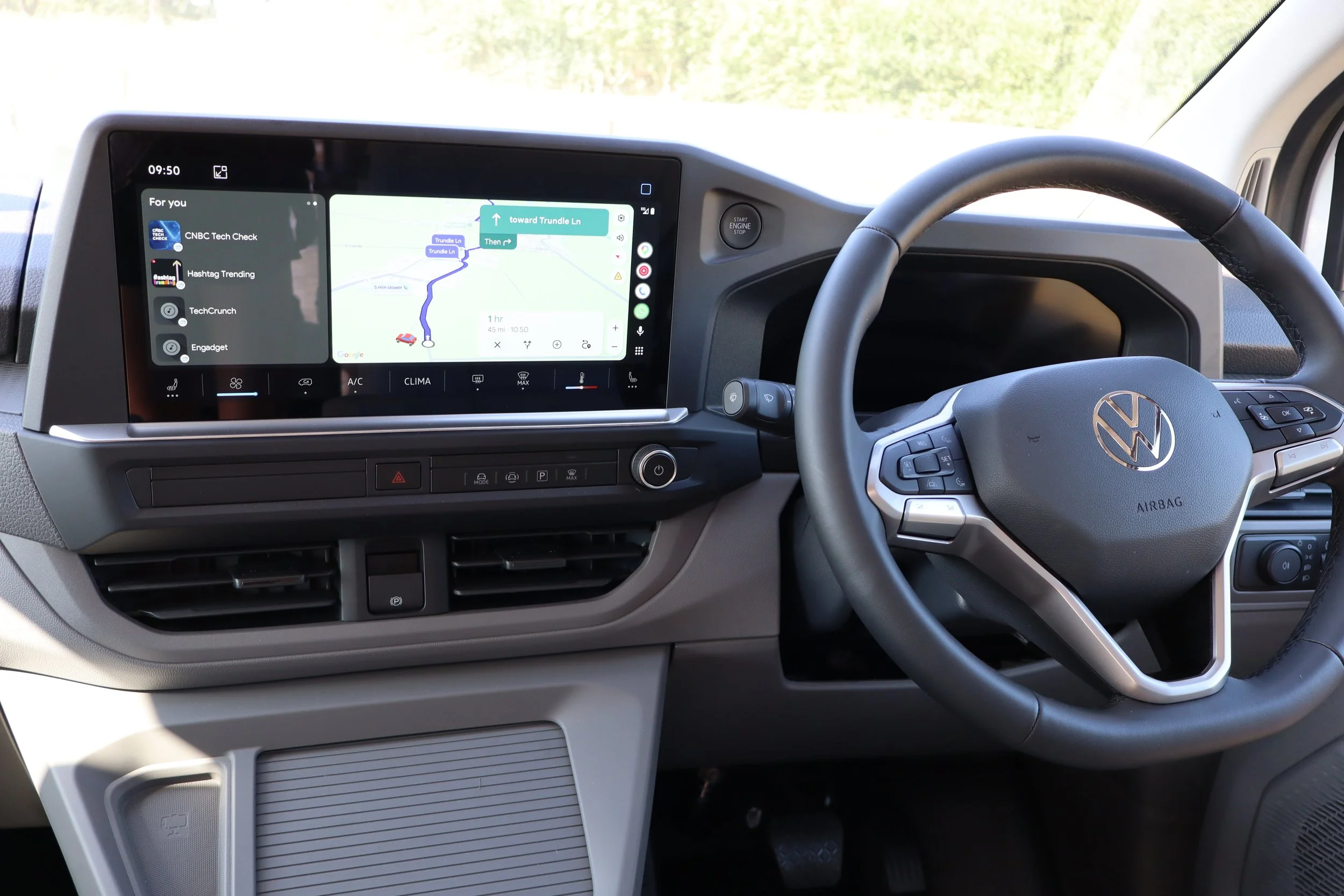 Interior of a Volkswagen vehicle showing the dashboard, steering wheel with VW logo, and a digital infotainment screen displaying a navigation map and entertainment options.