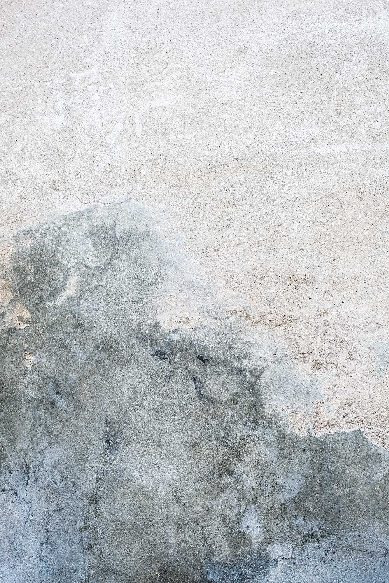 Superficie di muro di cemento con variazioni di colore e texture, inclusi crepe e segni di corrosione.