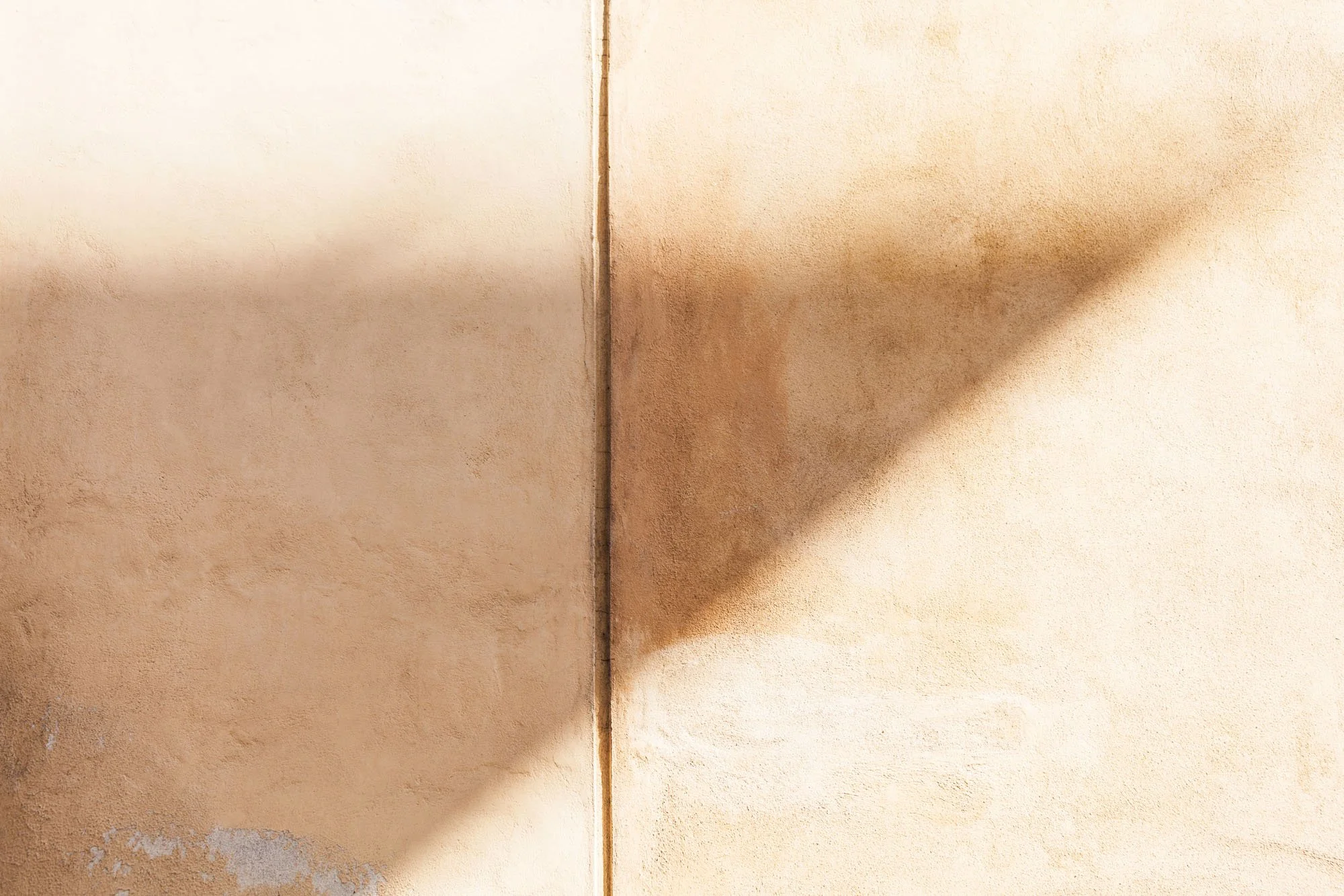 Superficie di due pareti di colore beige con una linea di divisione al centro, ombra proiettata sulla parete destra.