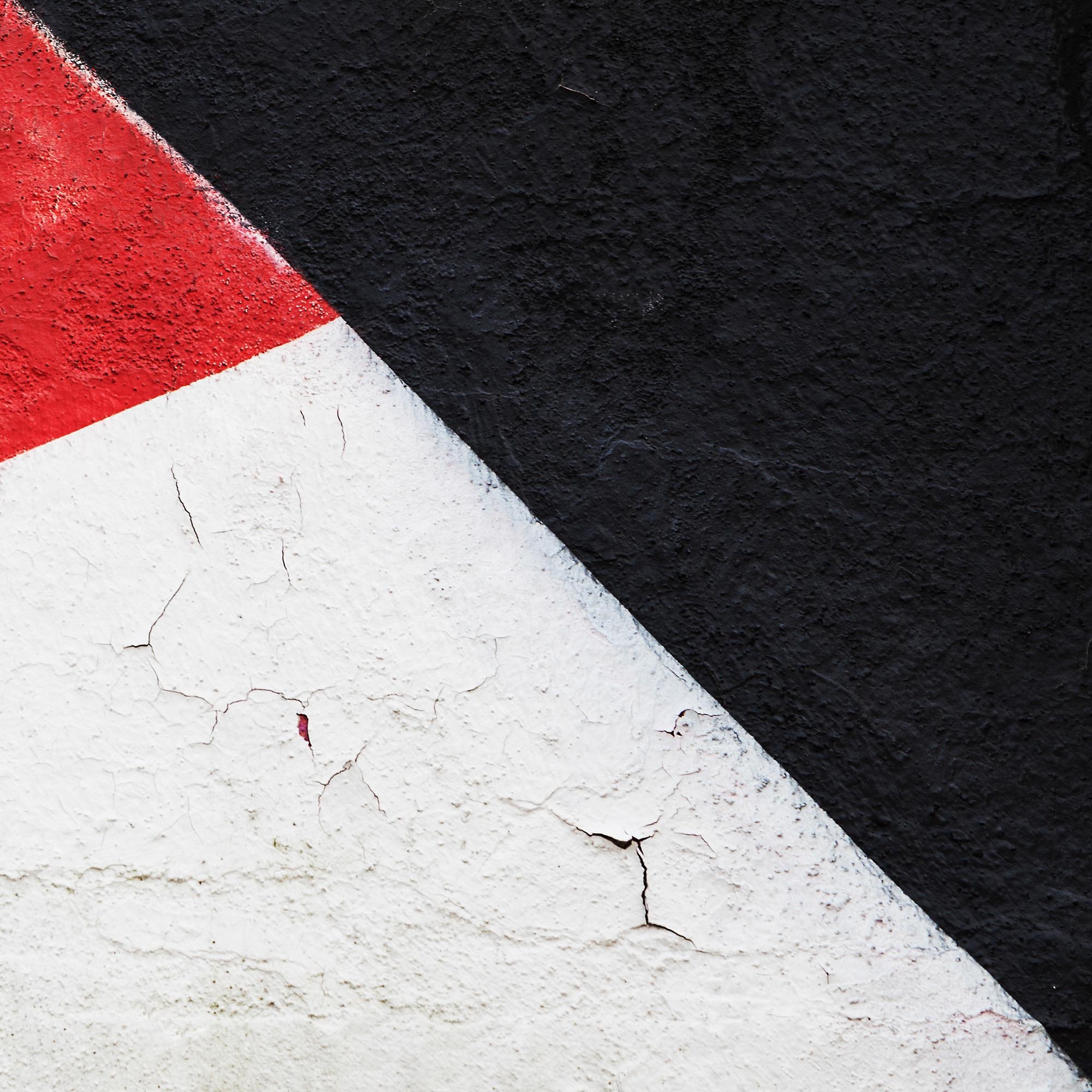 Parete dipinta con una geometria di colori bianco, rosso e nero, con alcune crepe sulla superficie del muro.