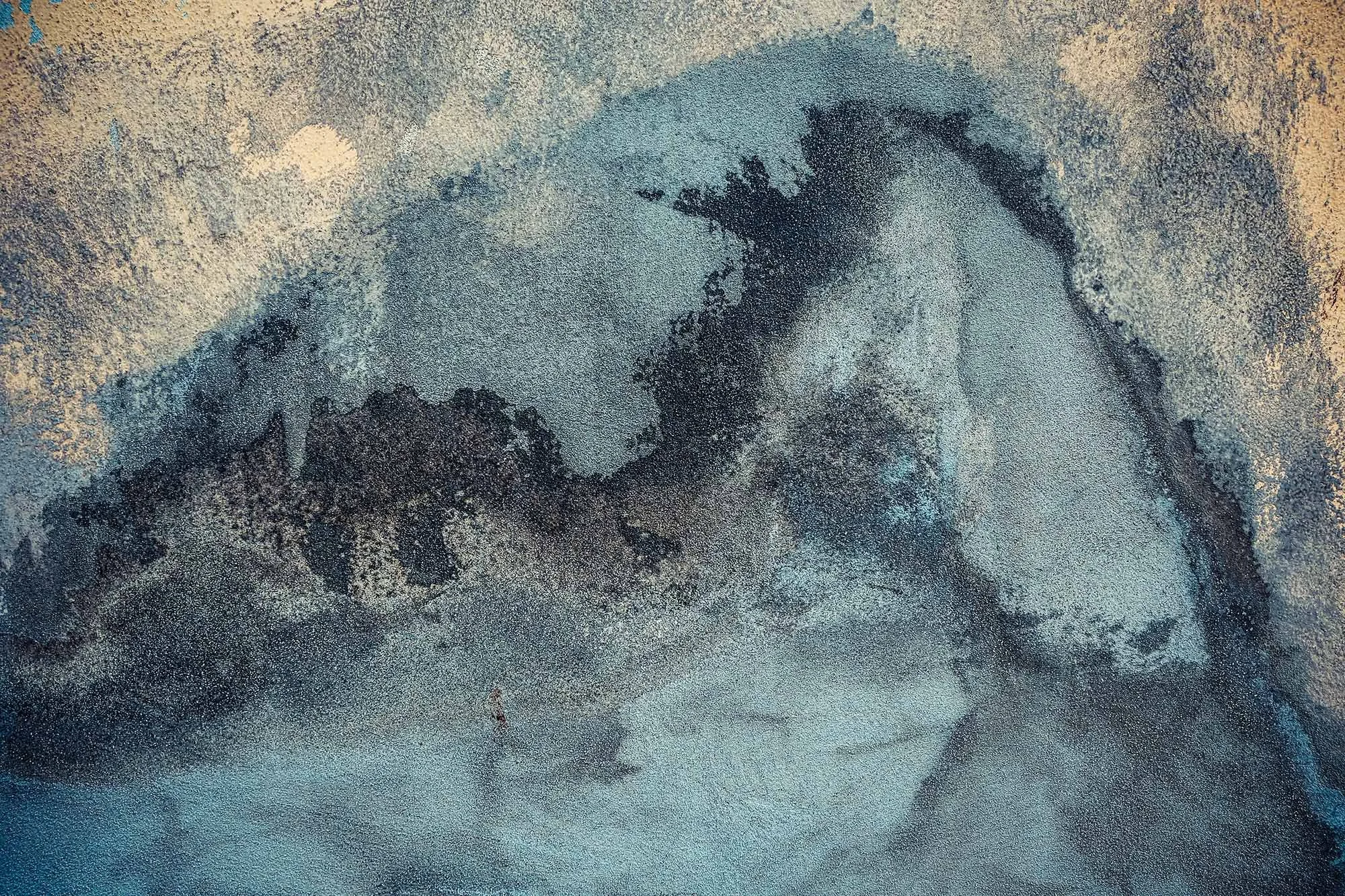 Una foto in colore di una superficie di terra e sabbia con variazioni di tonalità e alcune zone più scure. 