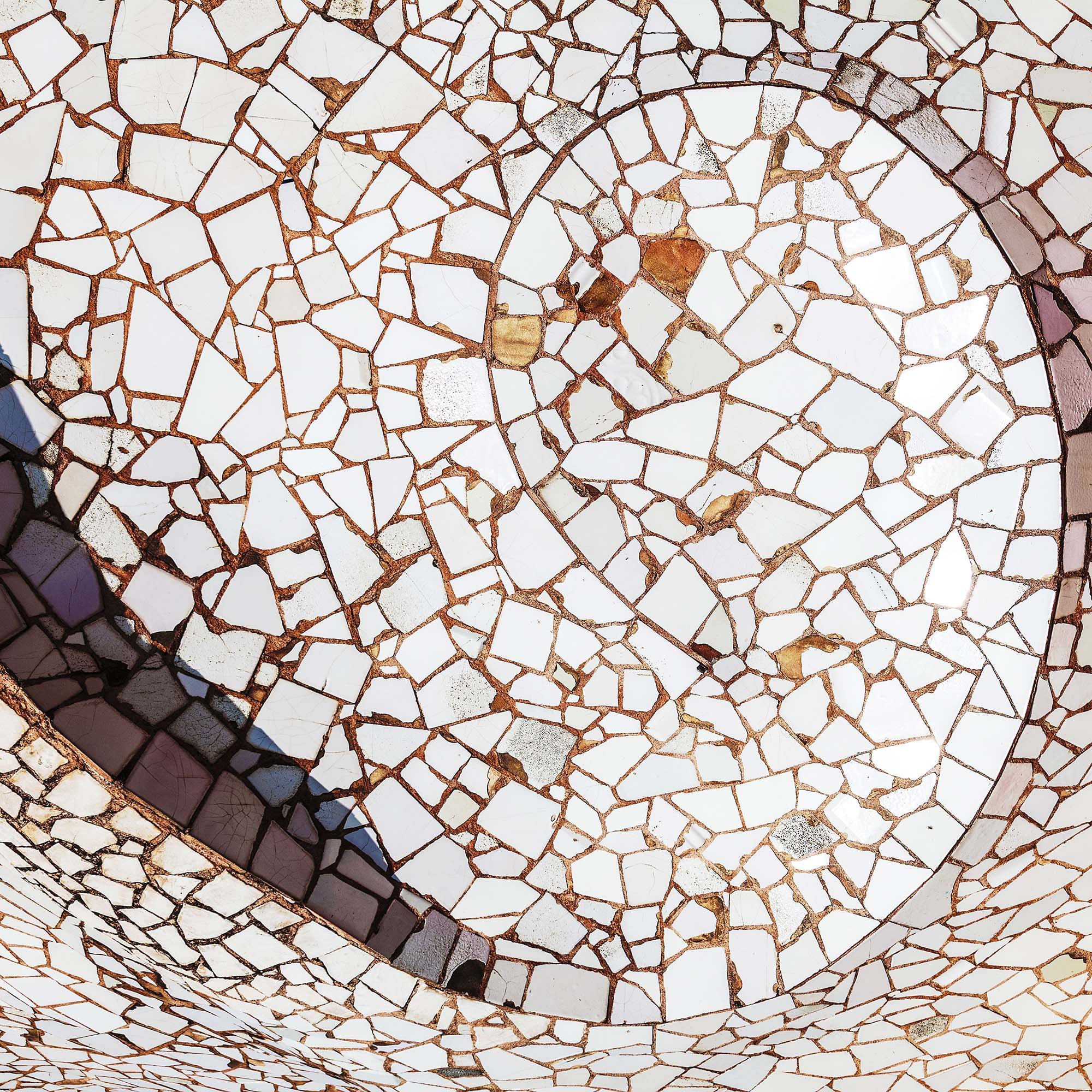 Particolare di una parete rivestita con piastrelle di mosaico bianco conFrance tiche di marmo e cemento, disposte in modo casuale e con alcuni frammenti di vetro.