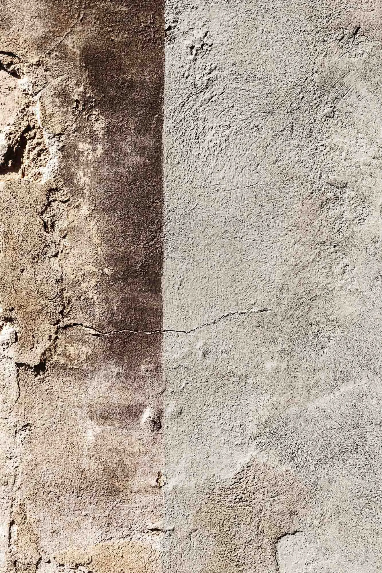 Superficie di muro di cemento con crepe e imperfezioni, con una sezione più scura e ruvida a sinistra.